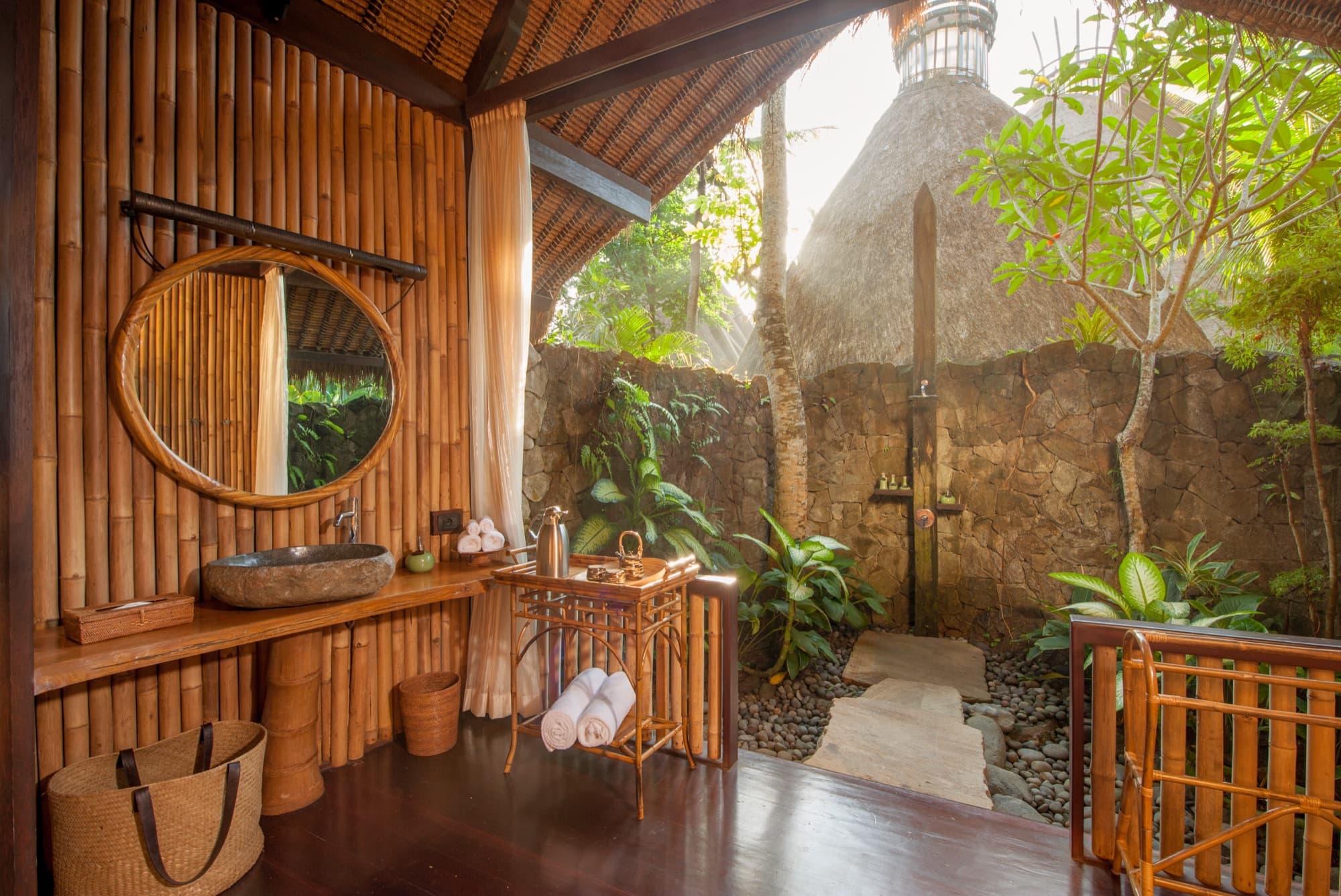 Outdoor bathroom with bamboo wall, stone shower and round mirror