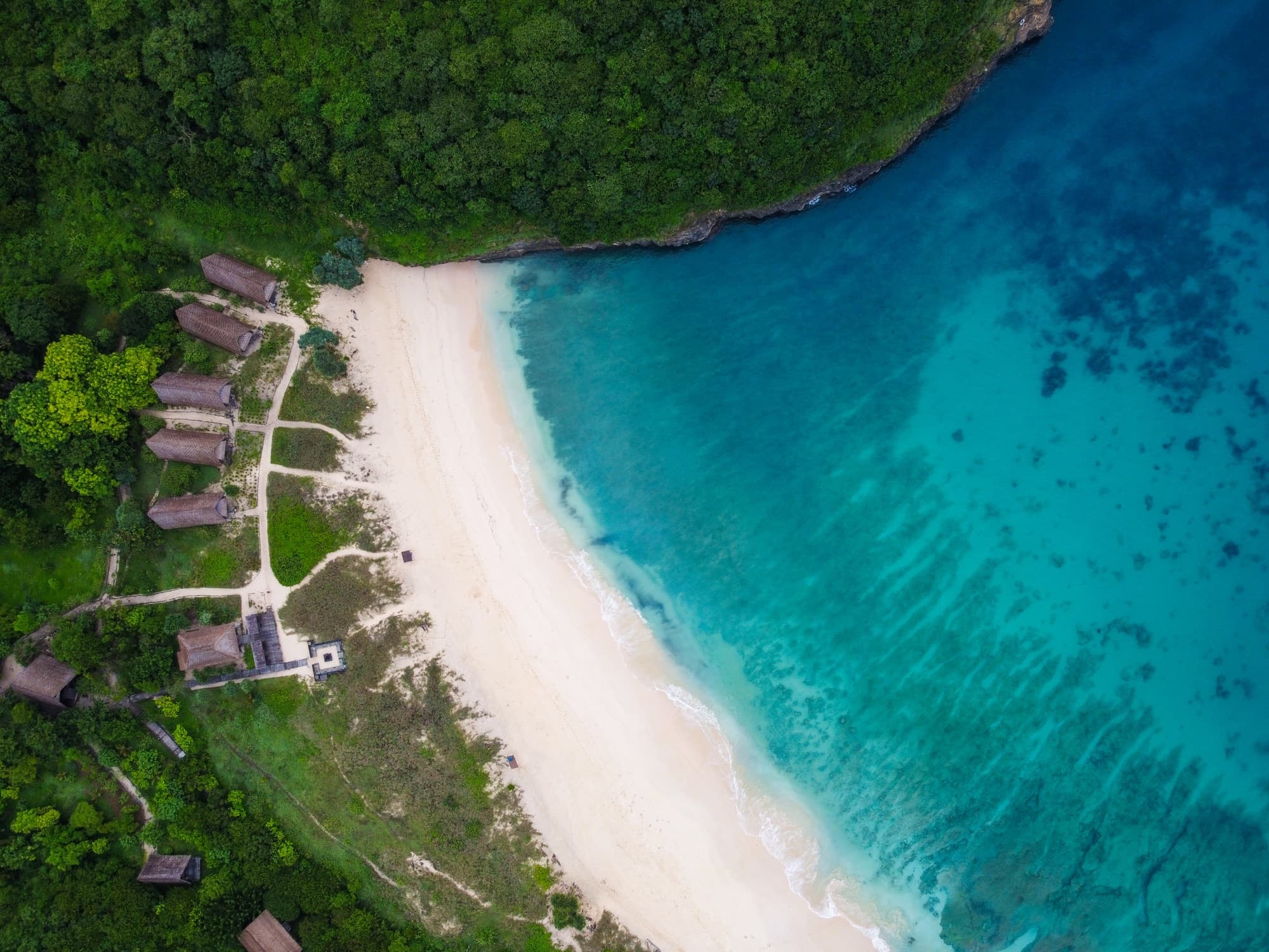 Aerial view of Jeeva Beloam Beach Camp from directly above — beach, A-frame lodges and turquoise sea, east Lombok