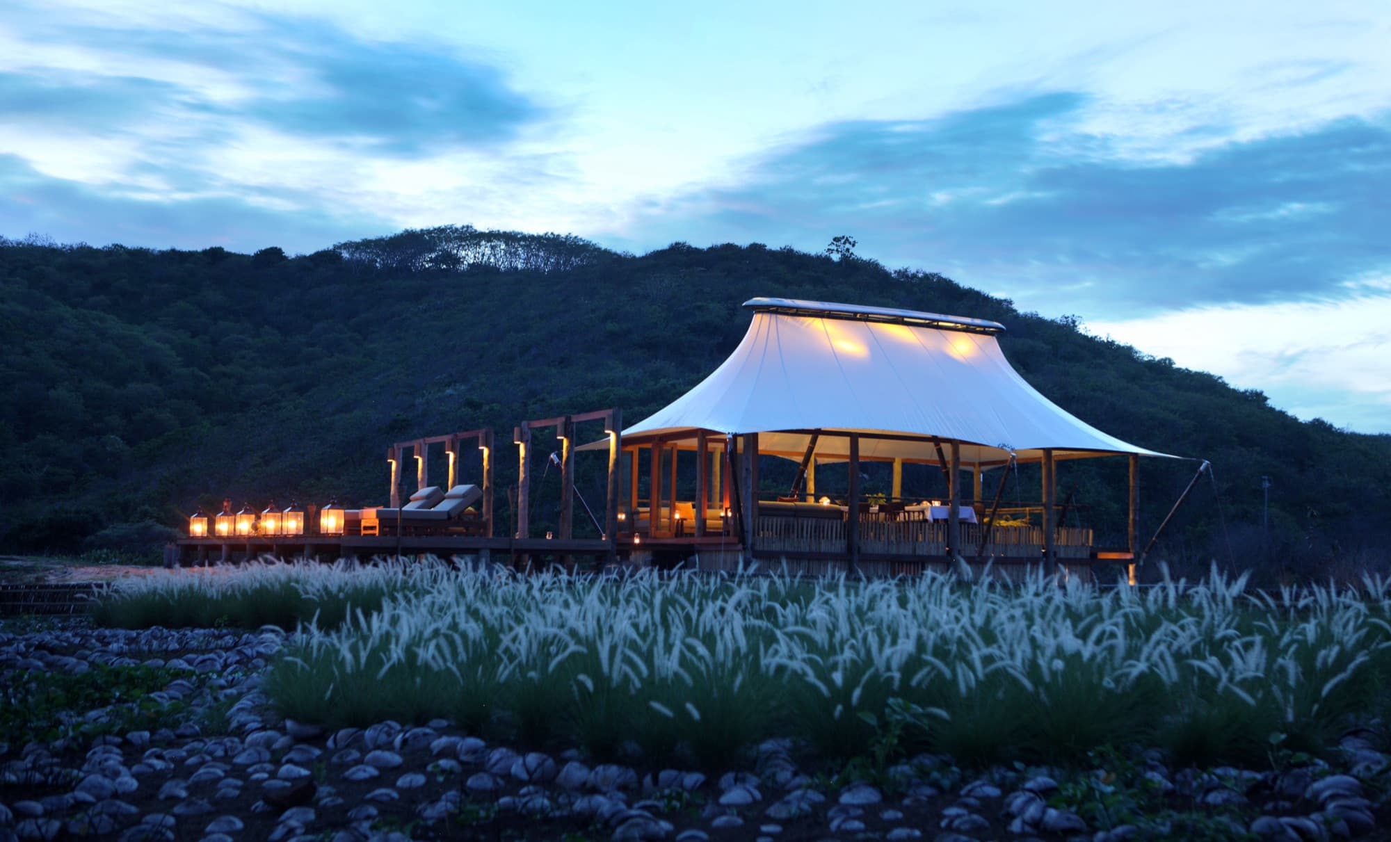 Dermaga restaurant terrace in the evening — open deck, fire pit seating and thatched pavilion