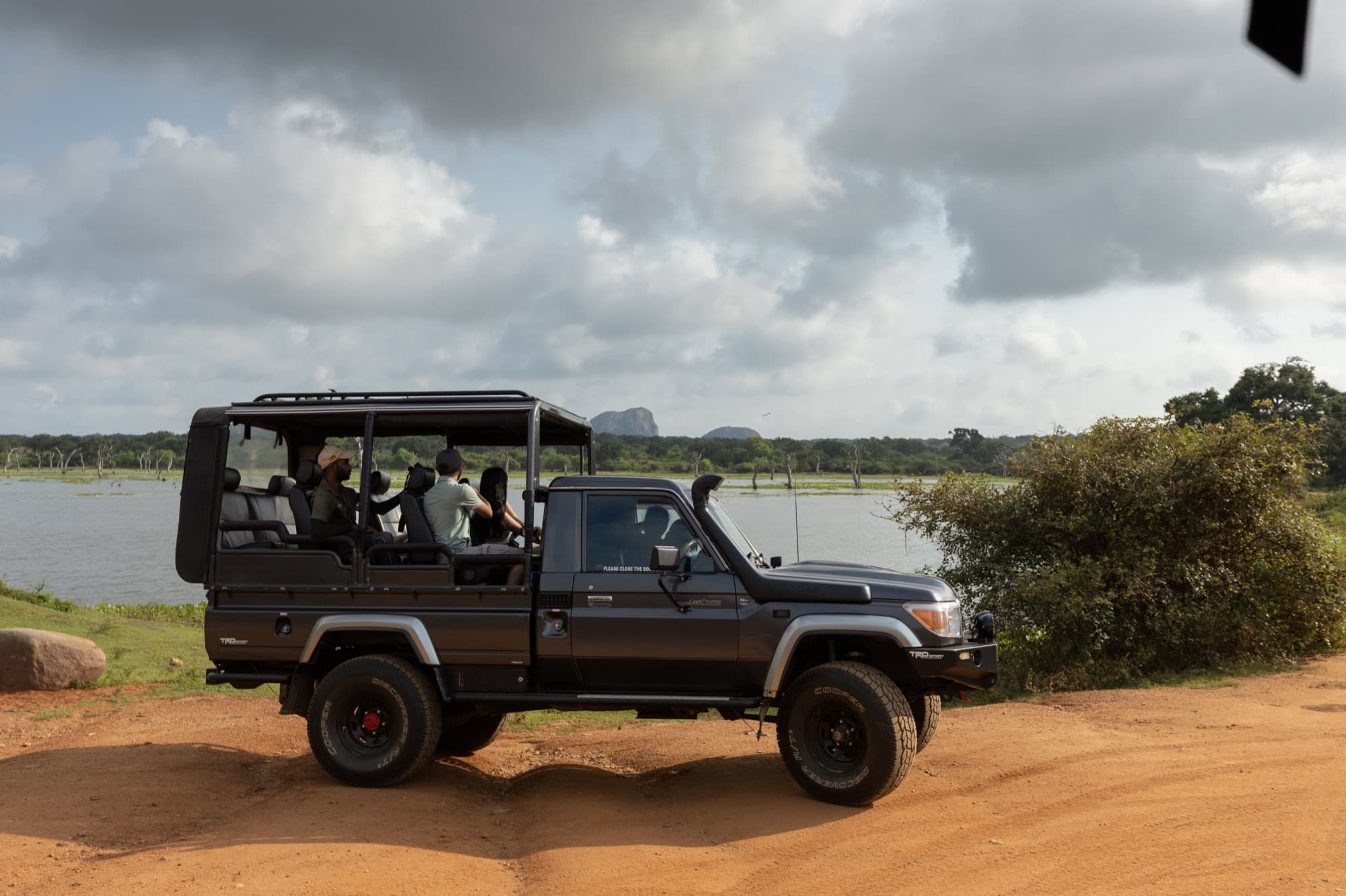 Safari jeep parked beside a Yala lagoon under a dramatic monsoon sky
