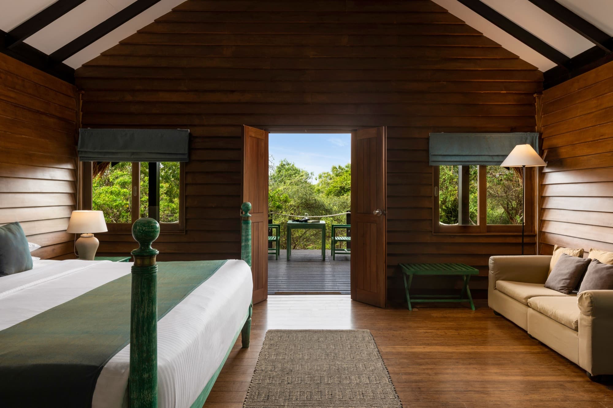 Wooden cabin bedroom with four-poster bed opening through double doors onto a private deck