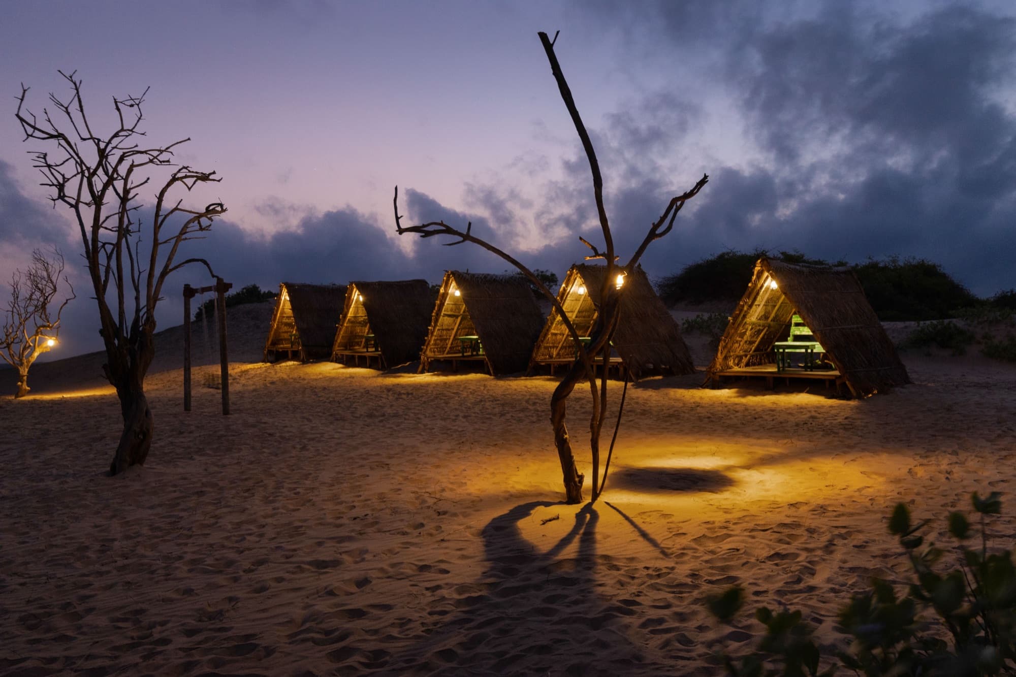 Row of lit thatched cabanas on the dune at twilight