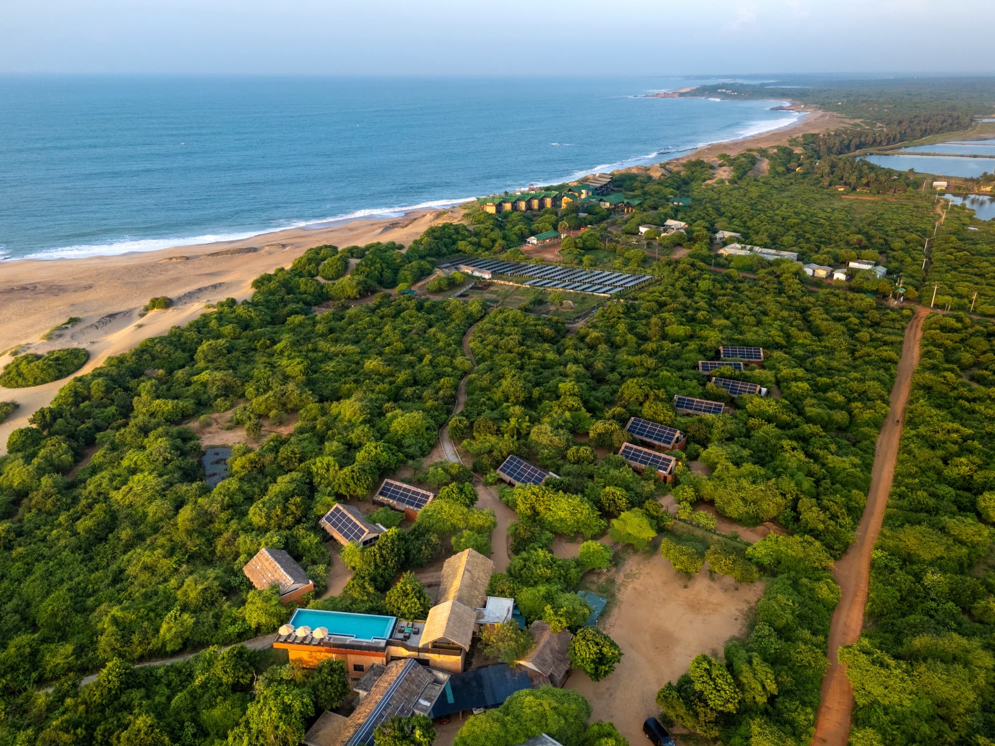 Aerial view of the lodge among coastal scrub with solar panels on cabin roofs and ocean beyond