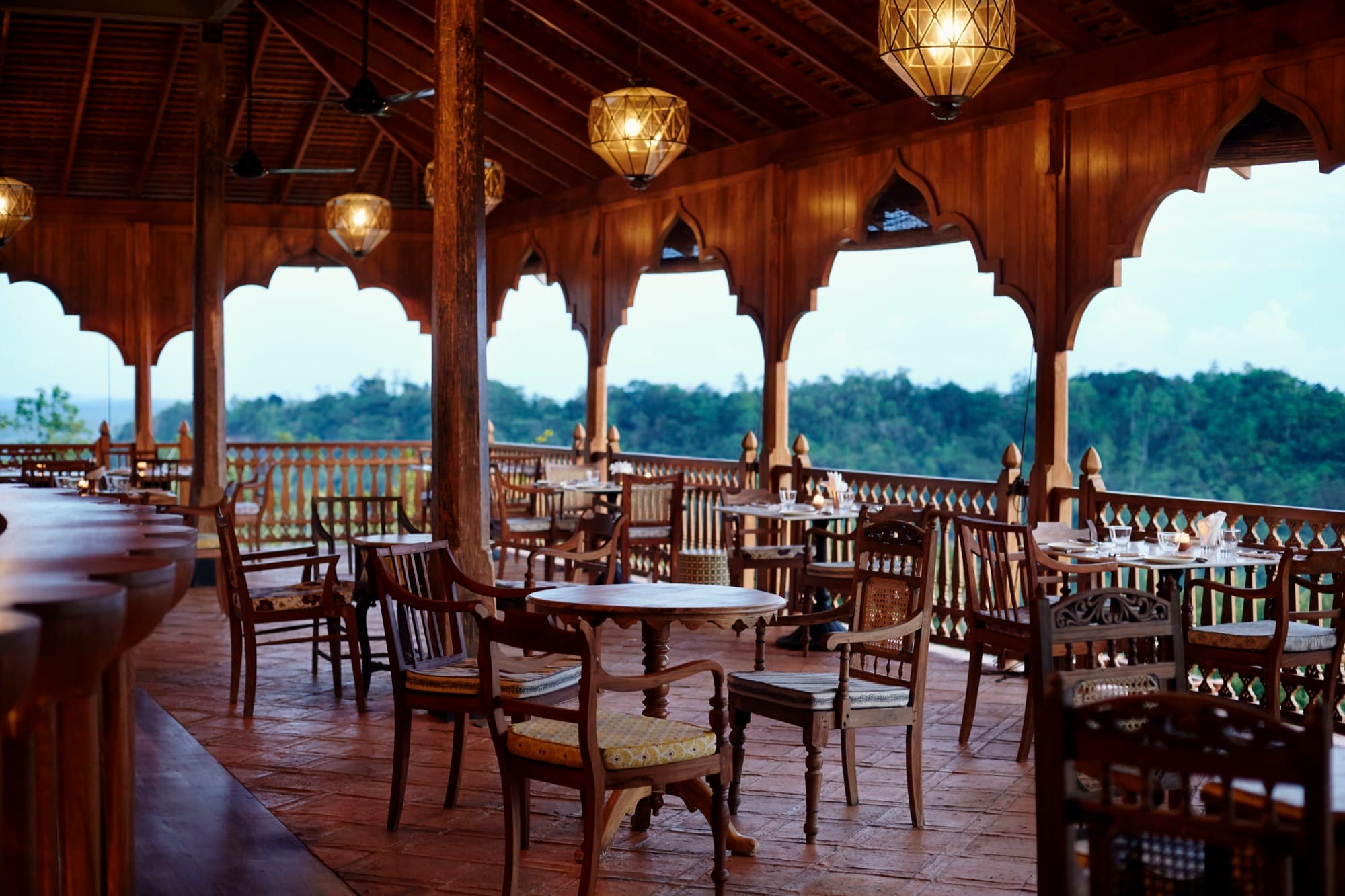 Timber restaurant terrace under Moorish arches at dusk, hills beyond