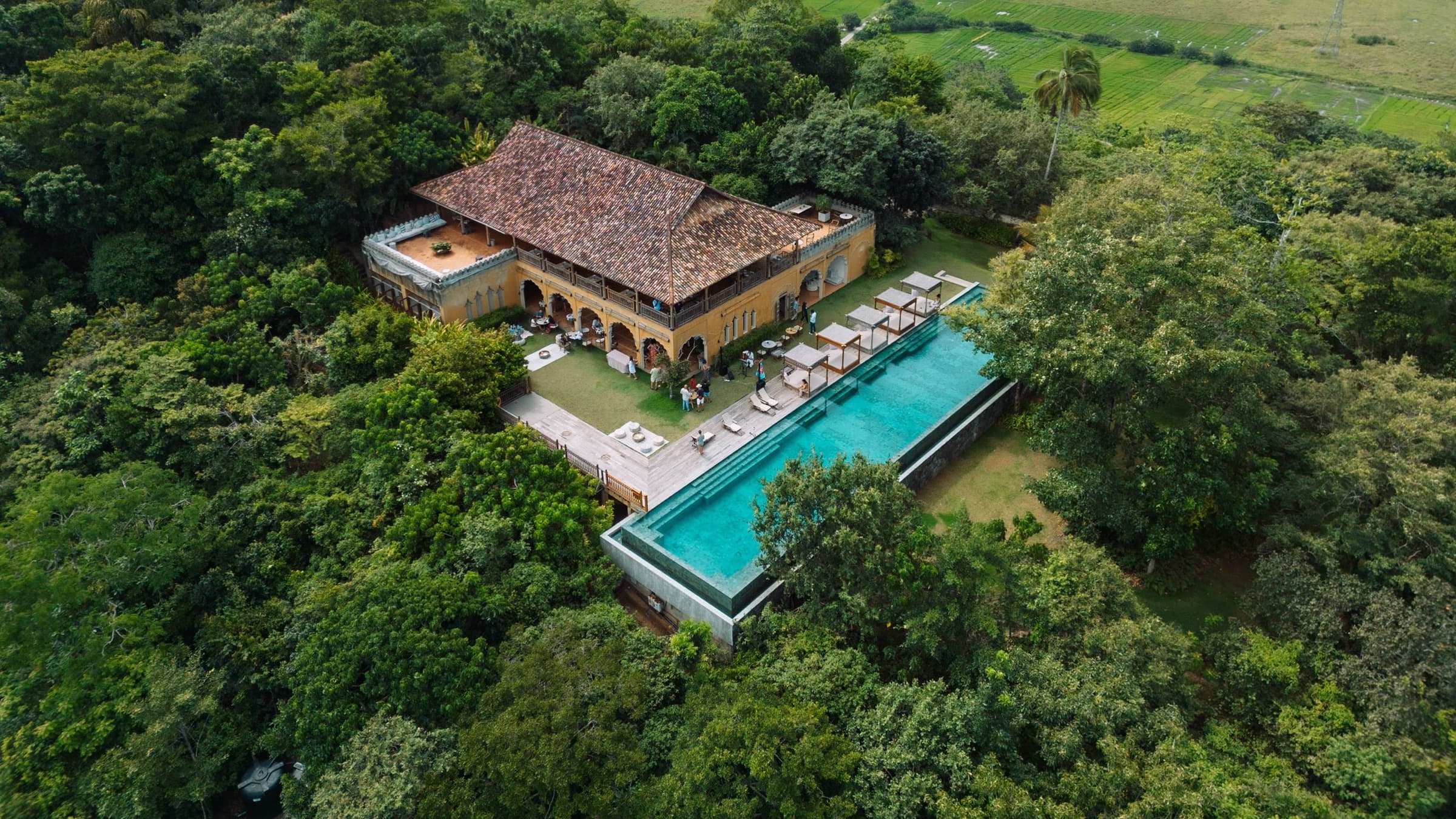 Aerial view of the Main House and 35-metre infinity pool on the forested hilltop, paddy fields beyond — Malabar Hill, near Weligama, Sri Lanka