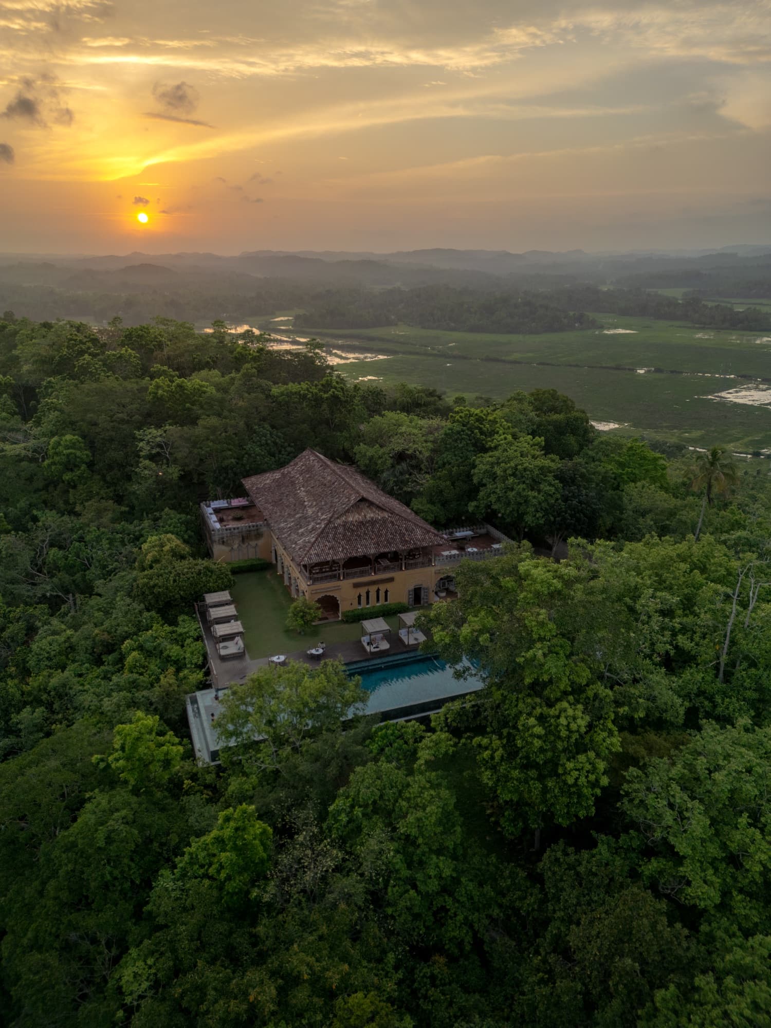 Aerial view of the Main House and pool on the forested ridge at sunset, wetlands beyond