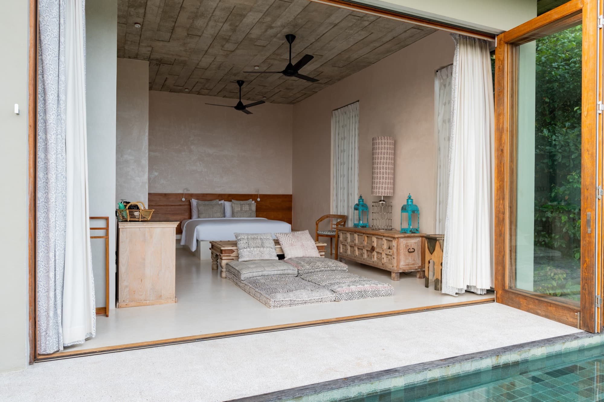 Villa bedroom opening through full-width doors onto the private plunge pool and jungle