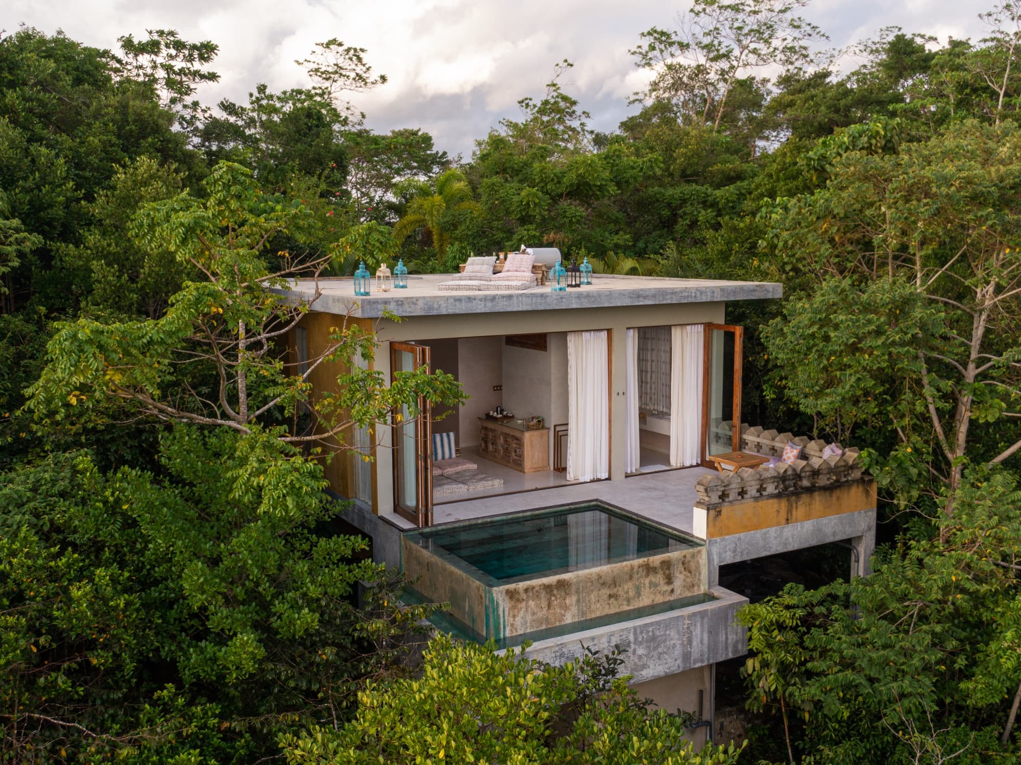 A glass-walled pool villa set into the forested hillside