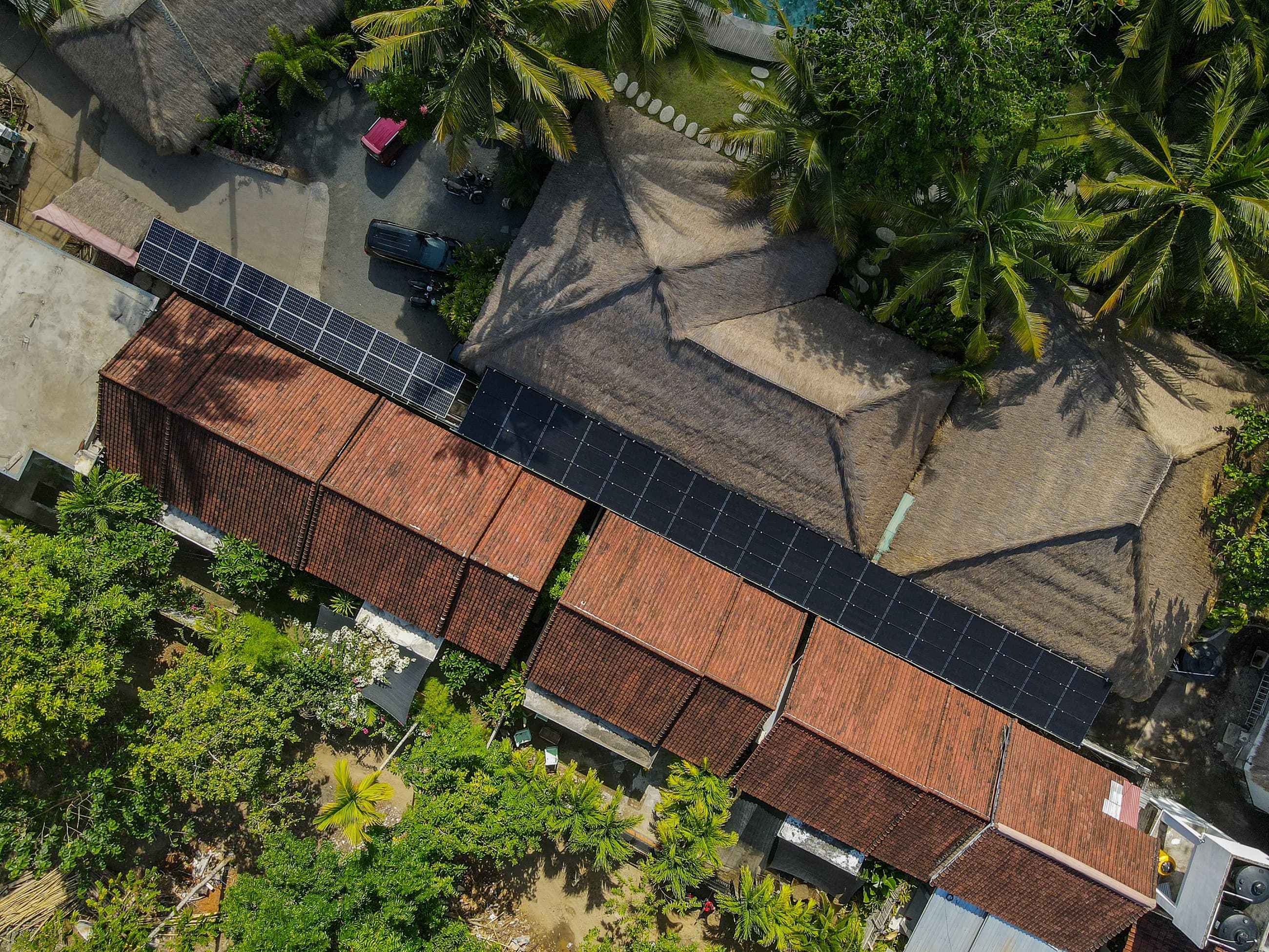 Vue aérienne des panneaux solaires couvrant les toits en tuiles et en chaume de Mana