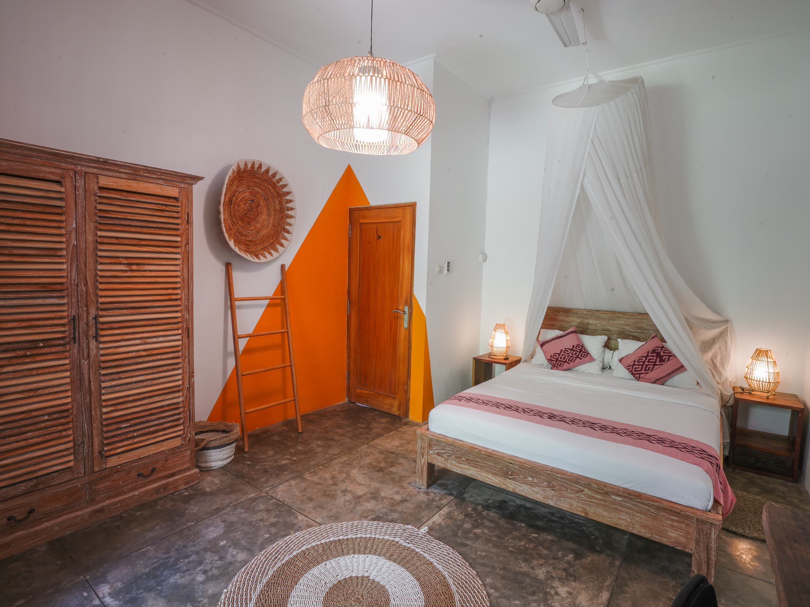 Chambre de la villa avec lit à baldaquin, mur orange et armoire en bois sculpté