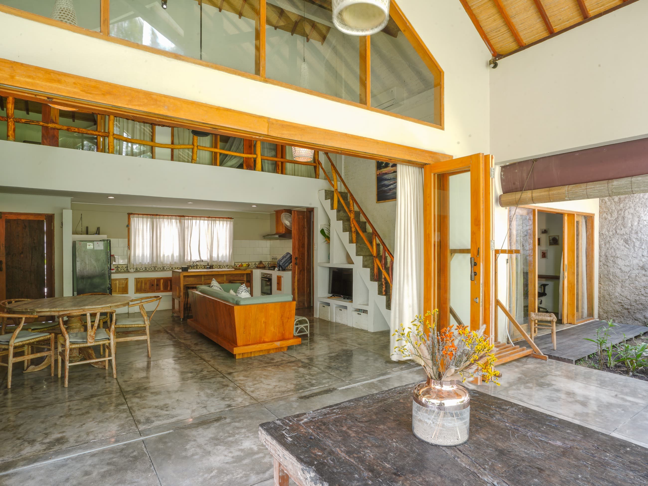 Séjour et salle à manger de la villa sous un plafond double hauteur, mezzanine et escalier ouvrant sur le jardin
