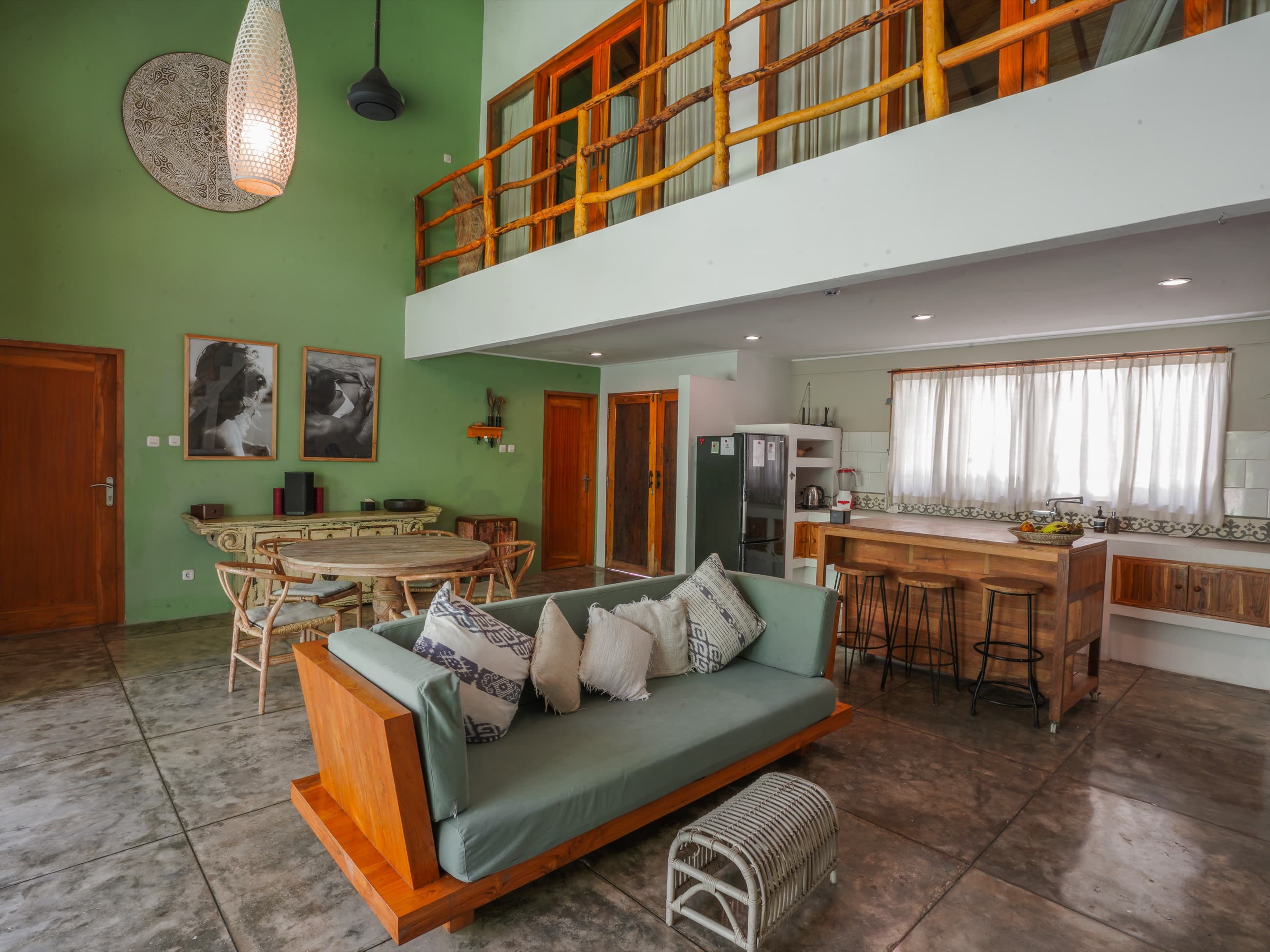 Salon de villa ouvert avec mur végétal, canapé en bois et mezzanine au-dessus d'un bar de cuisine