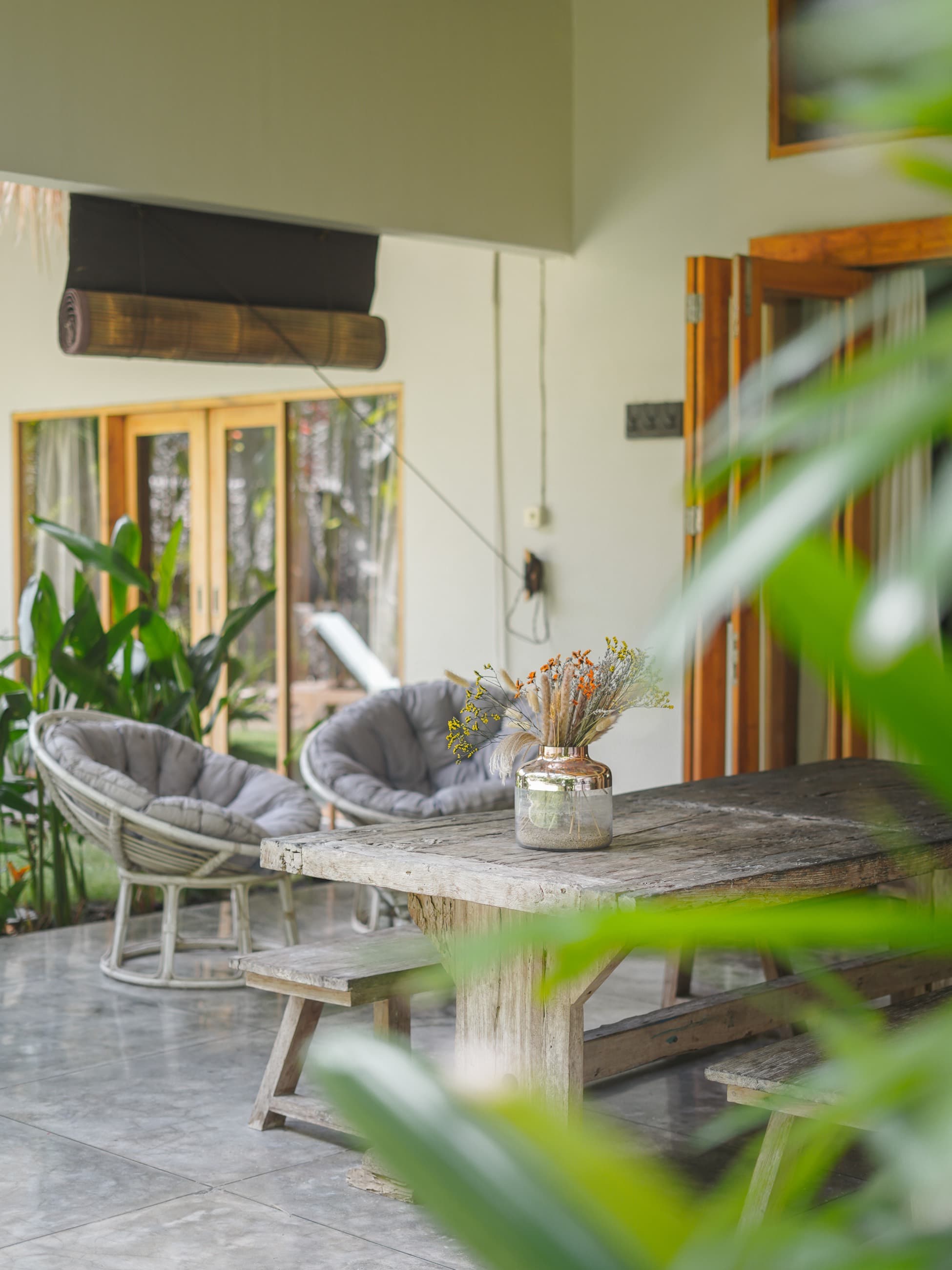 Terrasse couverte de la villa avec fauteuils papasan gris et table en bois patiné