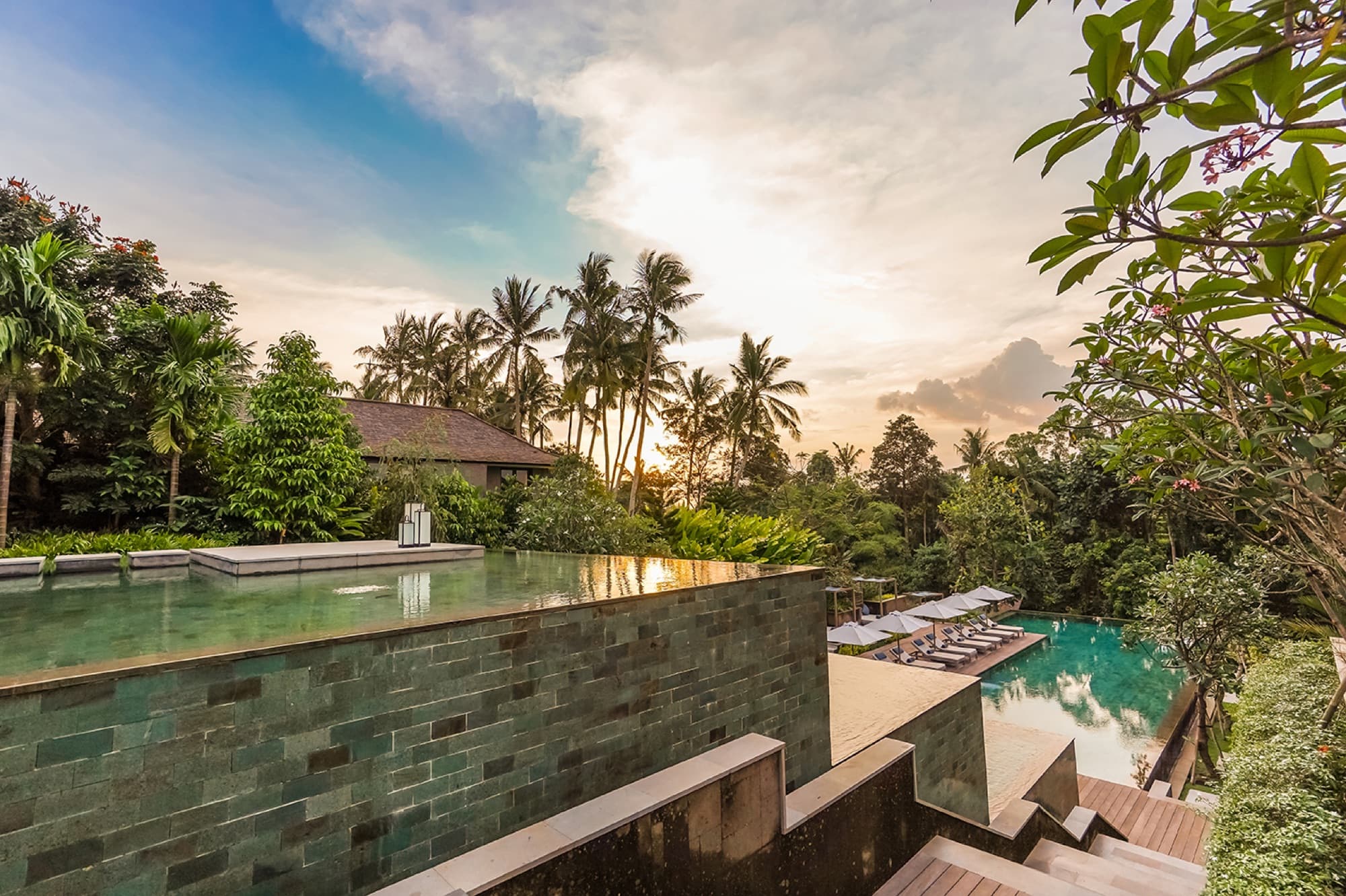 Green-tiled infinity pool at sunset overlooking palms and jungle