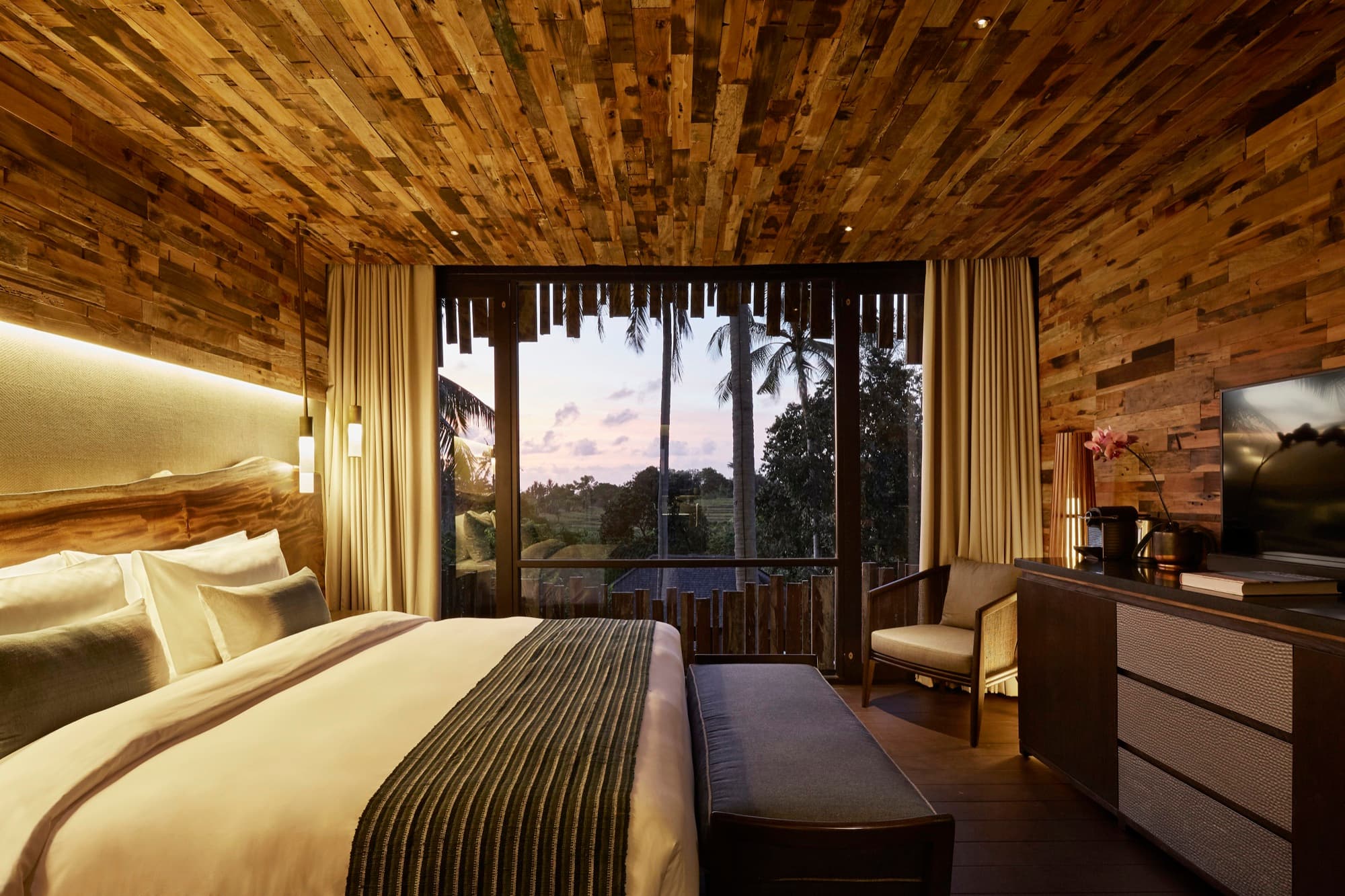 Canopy Suite bedroom with timber walls opening to rice fields at dusk