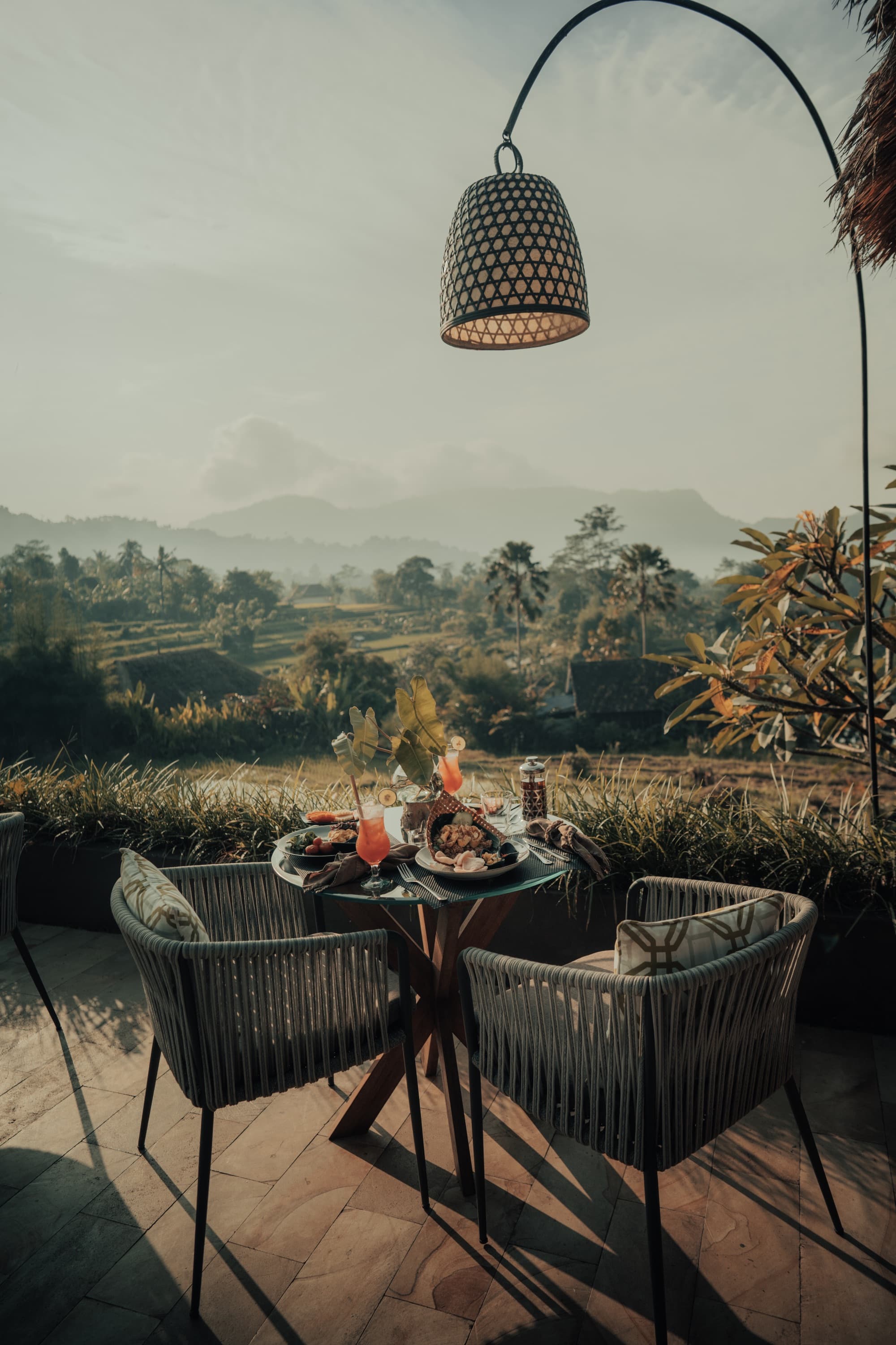 Outdoor dining table with cocktails overlooking Sidemen rice fields at dusk