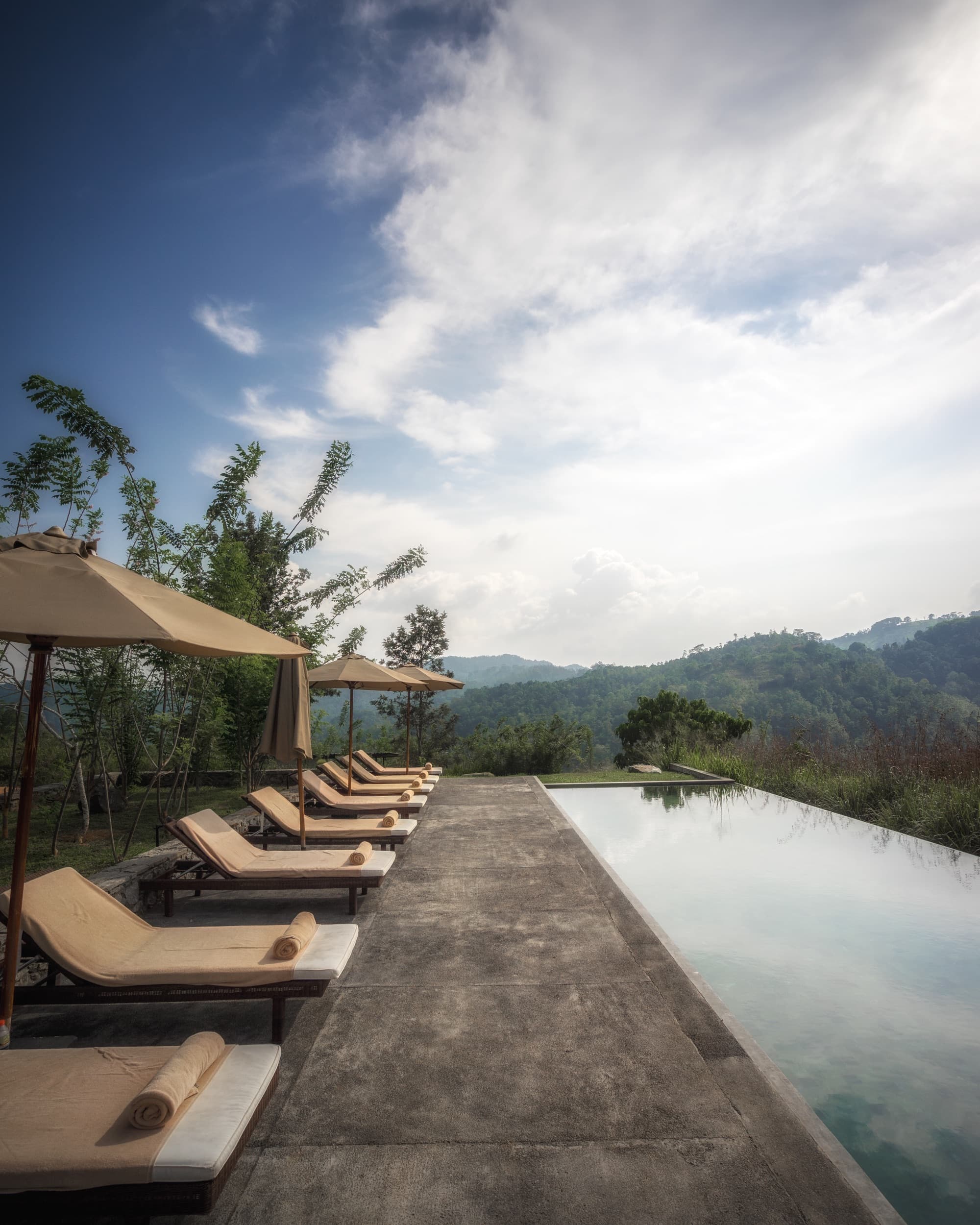 Row of loungers and parasols along the infinity pool under a bright mountain sky