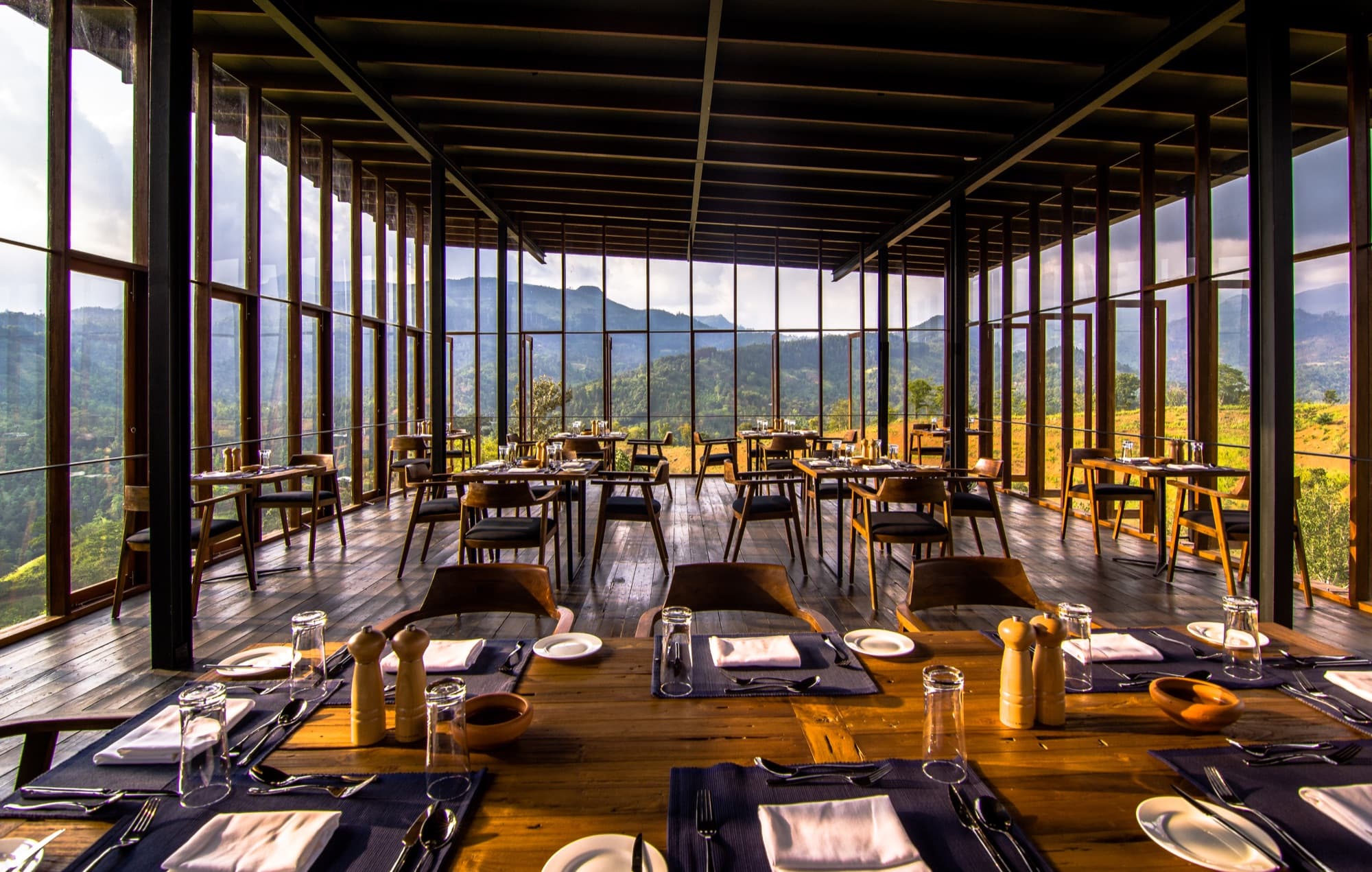 Glass-walled dining pavilion with set wooden tables overlooking the mountains and valley