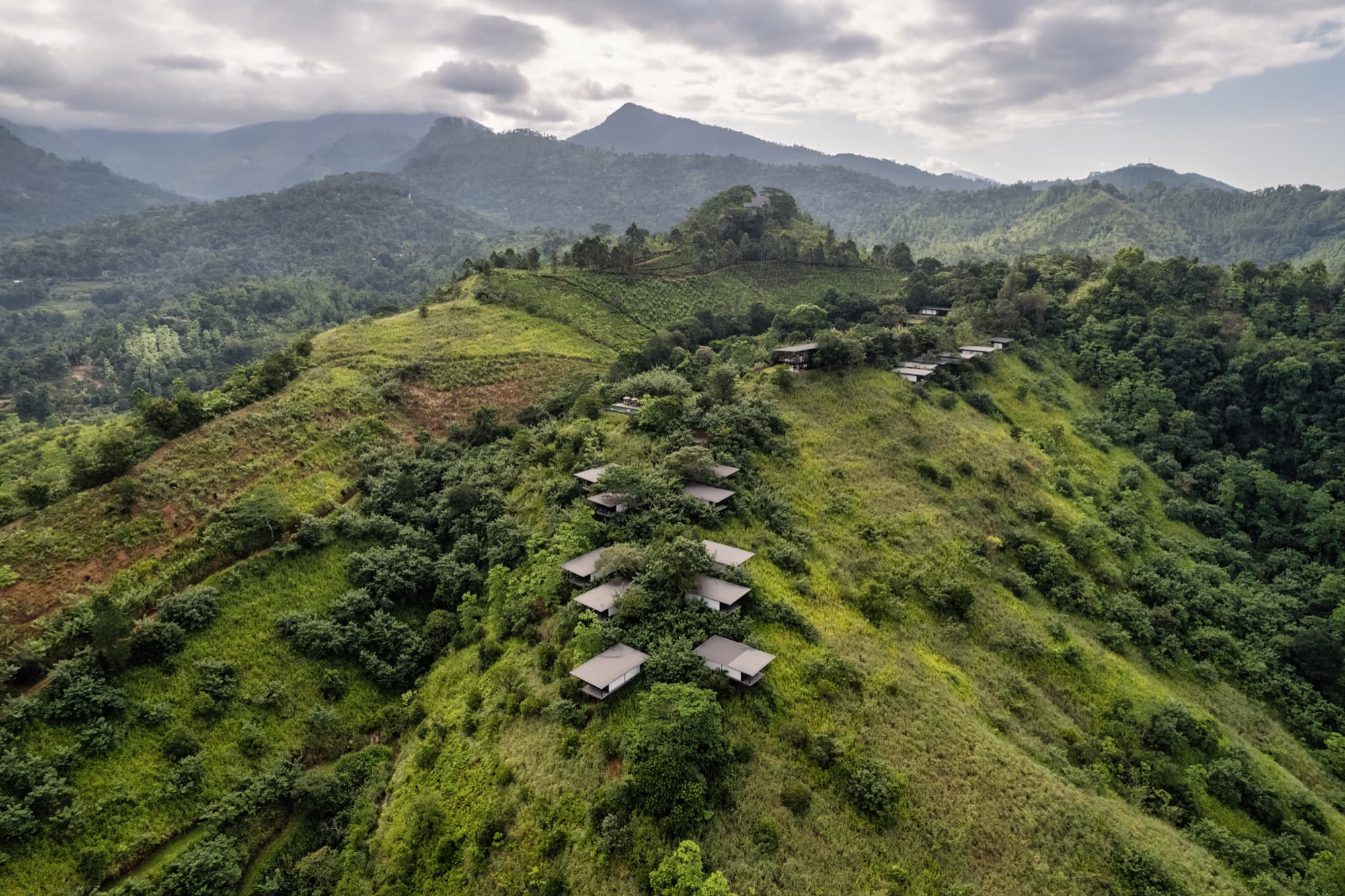 Aerial view of chalets scattered along a green ridge with mountains beyond
