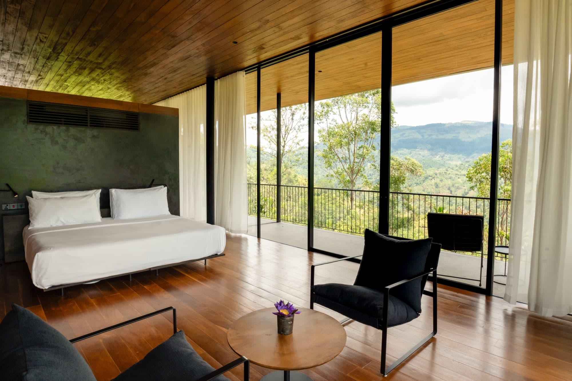 Villa bedroom with a low bed, timber floor and floor-to-ceiling glass onto the mountains