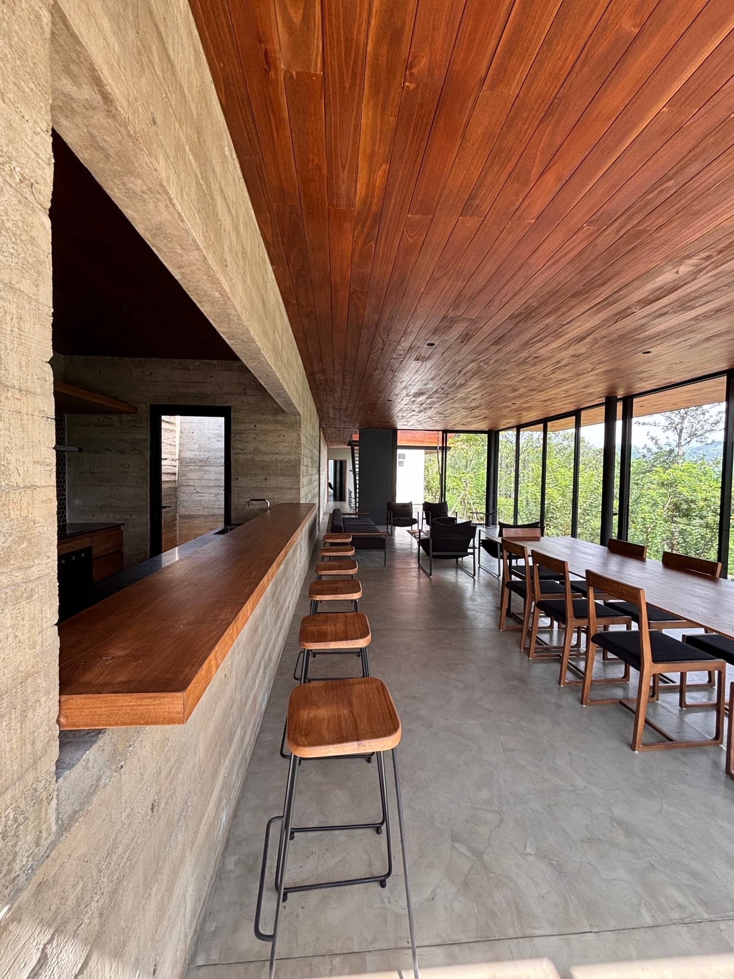Open-plan villa kitchen and bar counter in concrete and timber with stools and a glazed wall