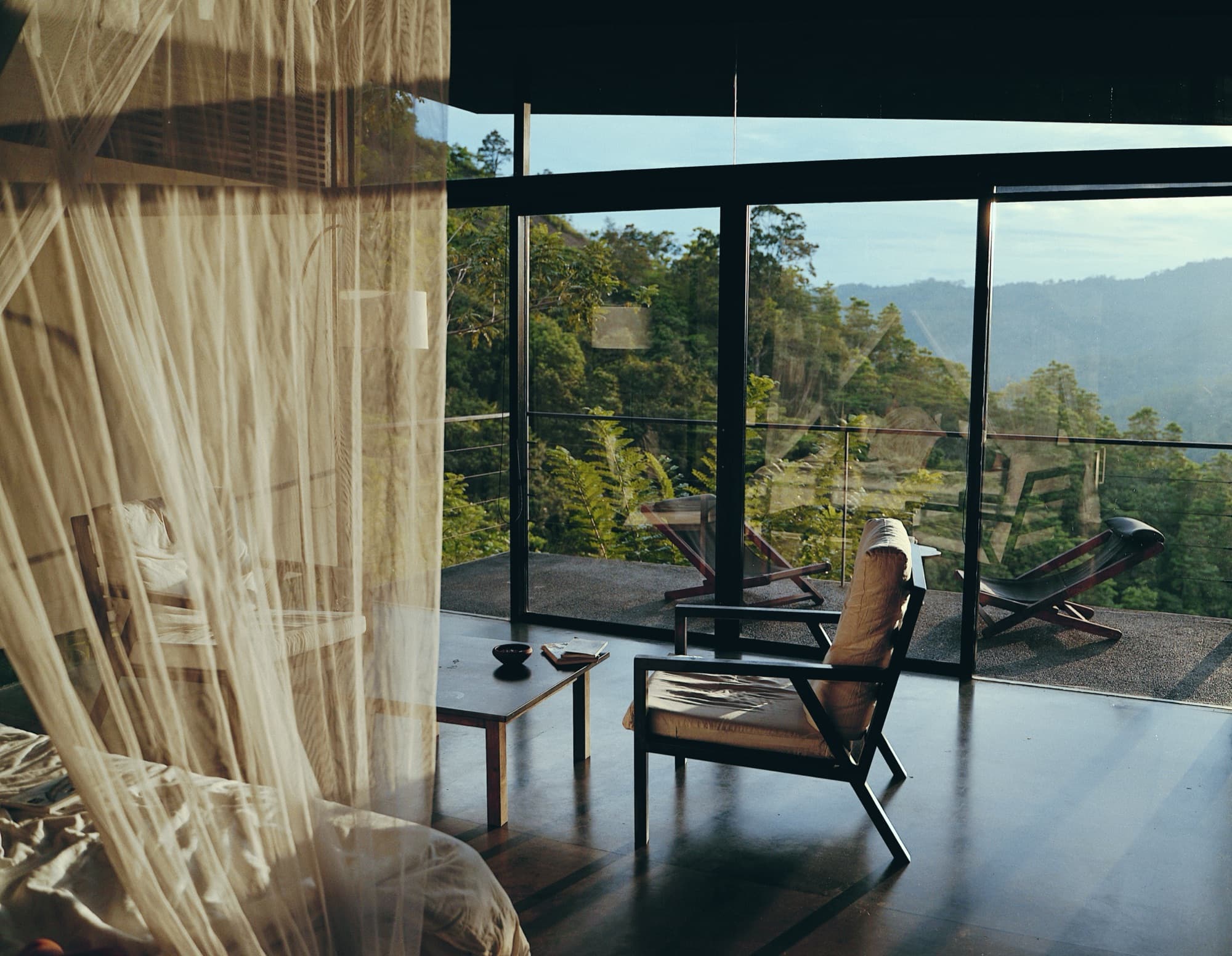 Chalet interior with a canopy-net bed and armchairs opening to a terrace over the valley