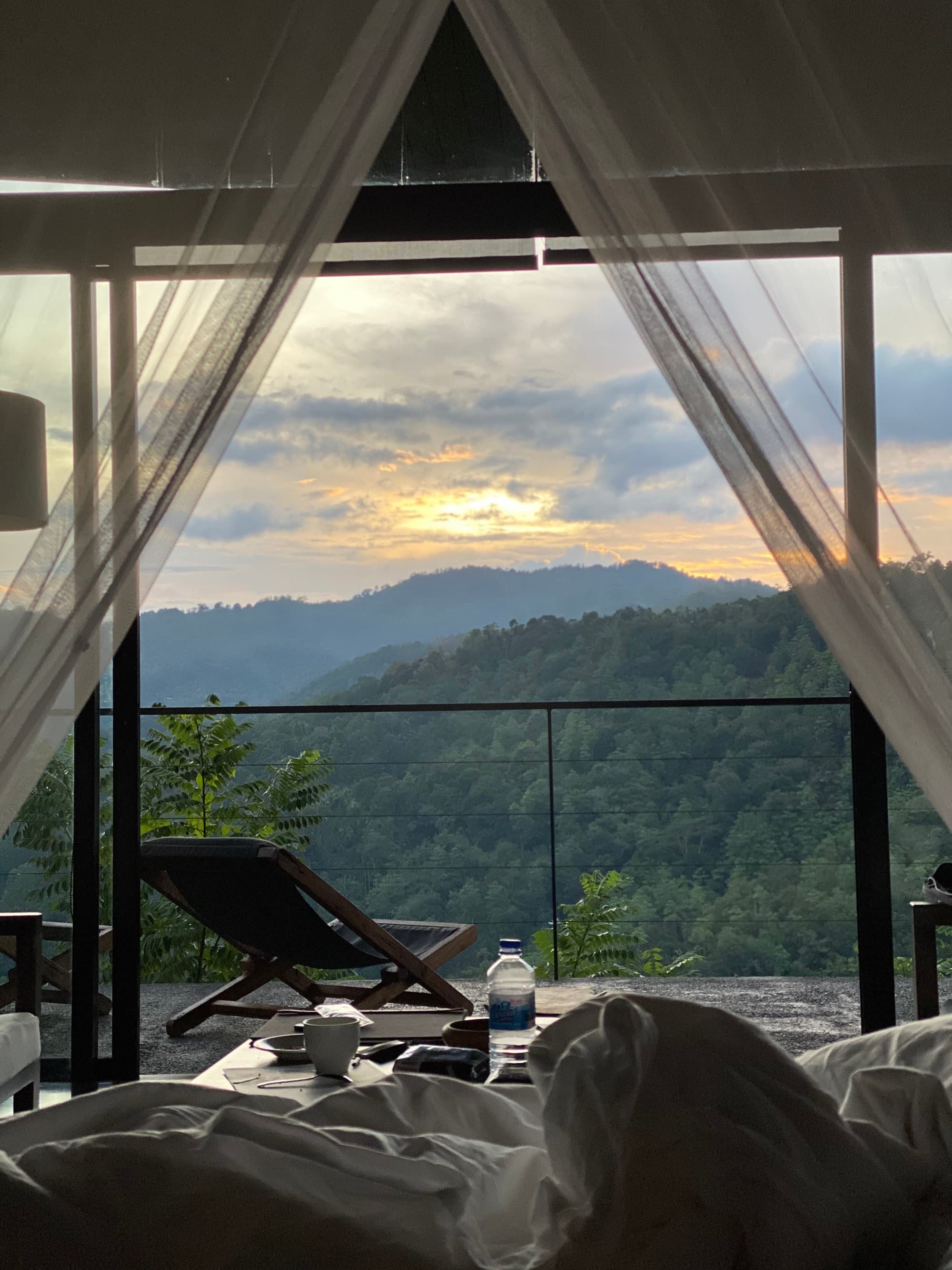 View from a chalet bed through the mosquito net to loungers and mountains at sunrise
