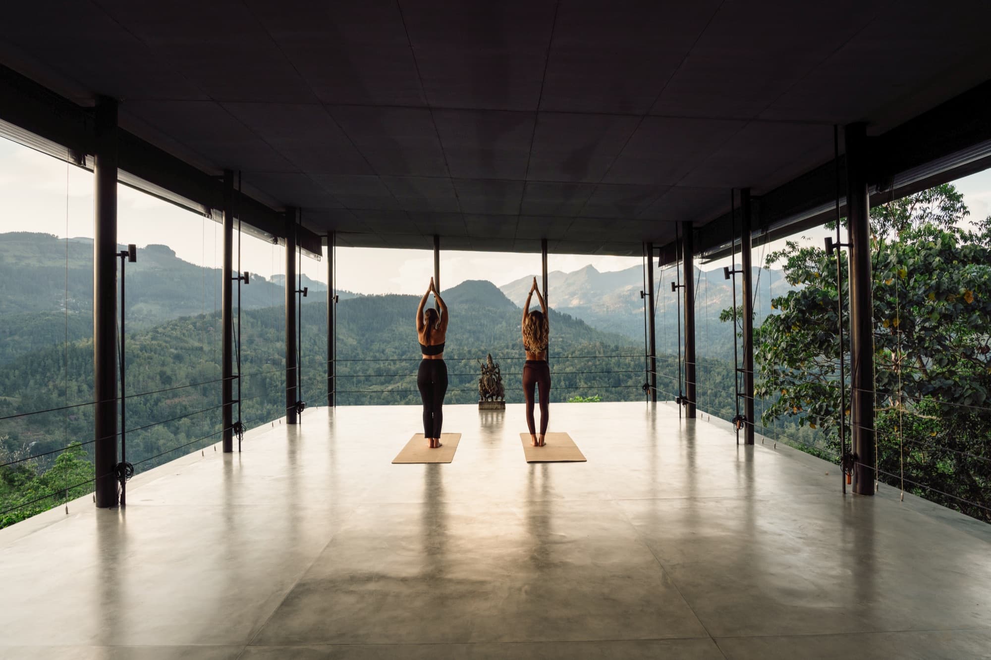 Two guests practising yoga in the open glass Surya Shala pavilion facing the mountains