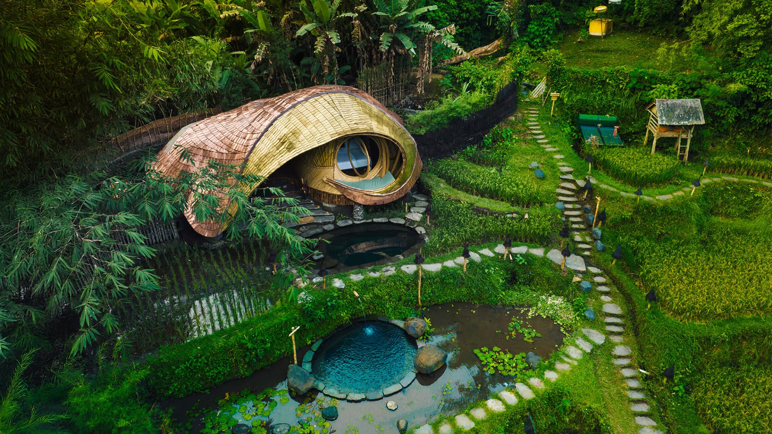 Aerial view of a bamboo house with round spring-fed plunge pools among rice terraces — Bambu Indah, Sayan Ridge near Ubud, Bali