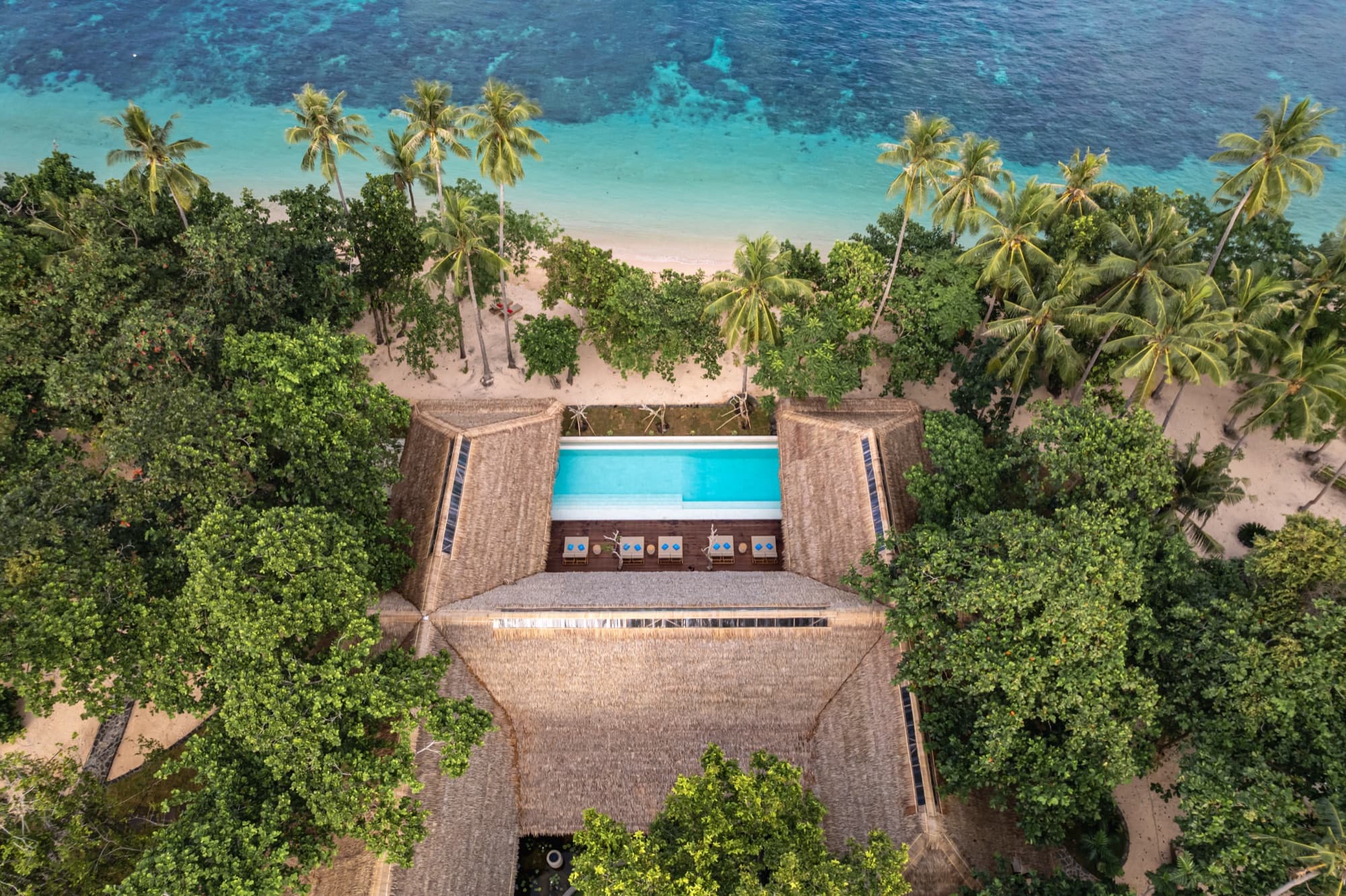 Sun loungers under a thatched roof beside the pool at Coral Eye, Bangka Island