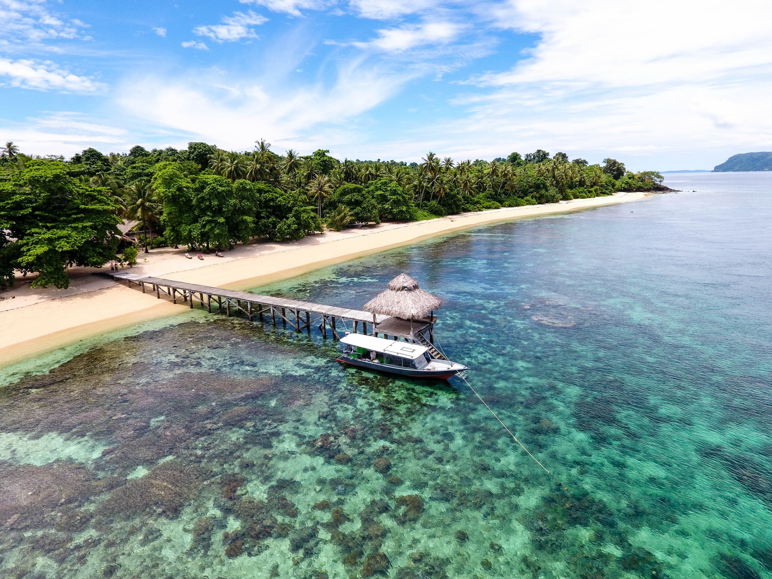 Aerial view of the Coral Eye jetty and boat over the turquoise house reef, Bangka Island, North Sulawesi