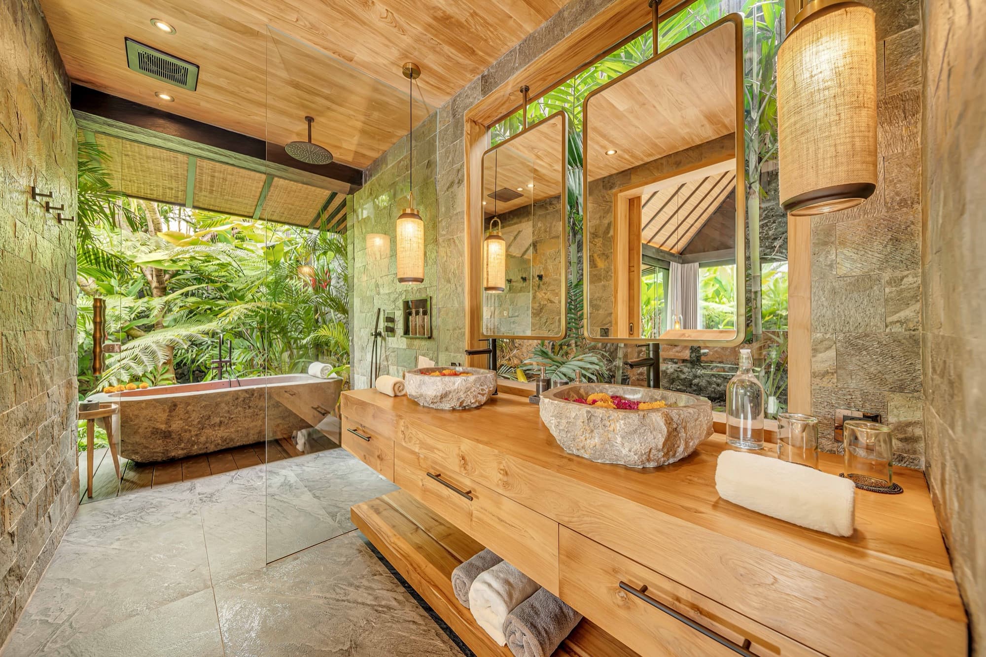 Villa bathroom in stone with twin basins and an open-air bathtub framed by jungle