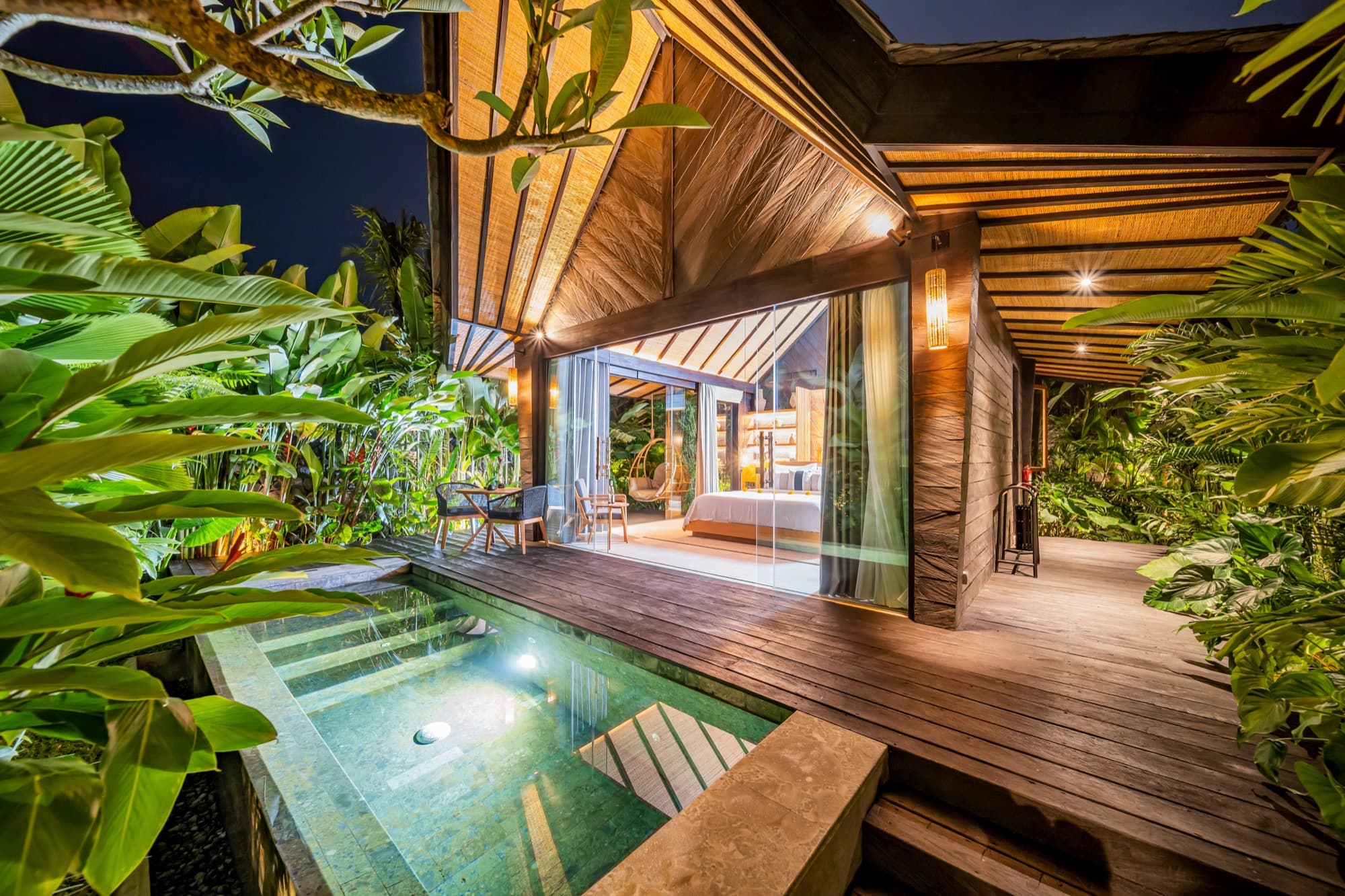 Villa lit at night, open to its deck and private plunge pool surrounded by greenery