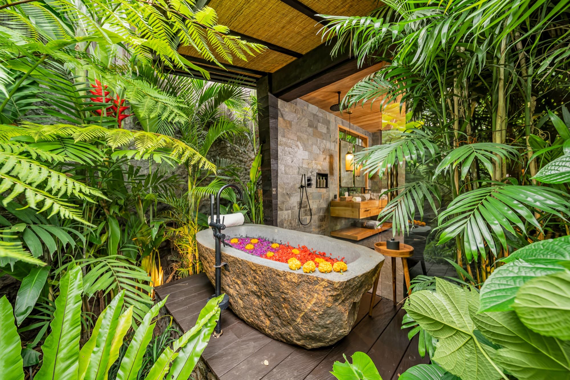 Stone bathtub scattered with flower petals on an open-air deck surrounded by jungle