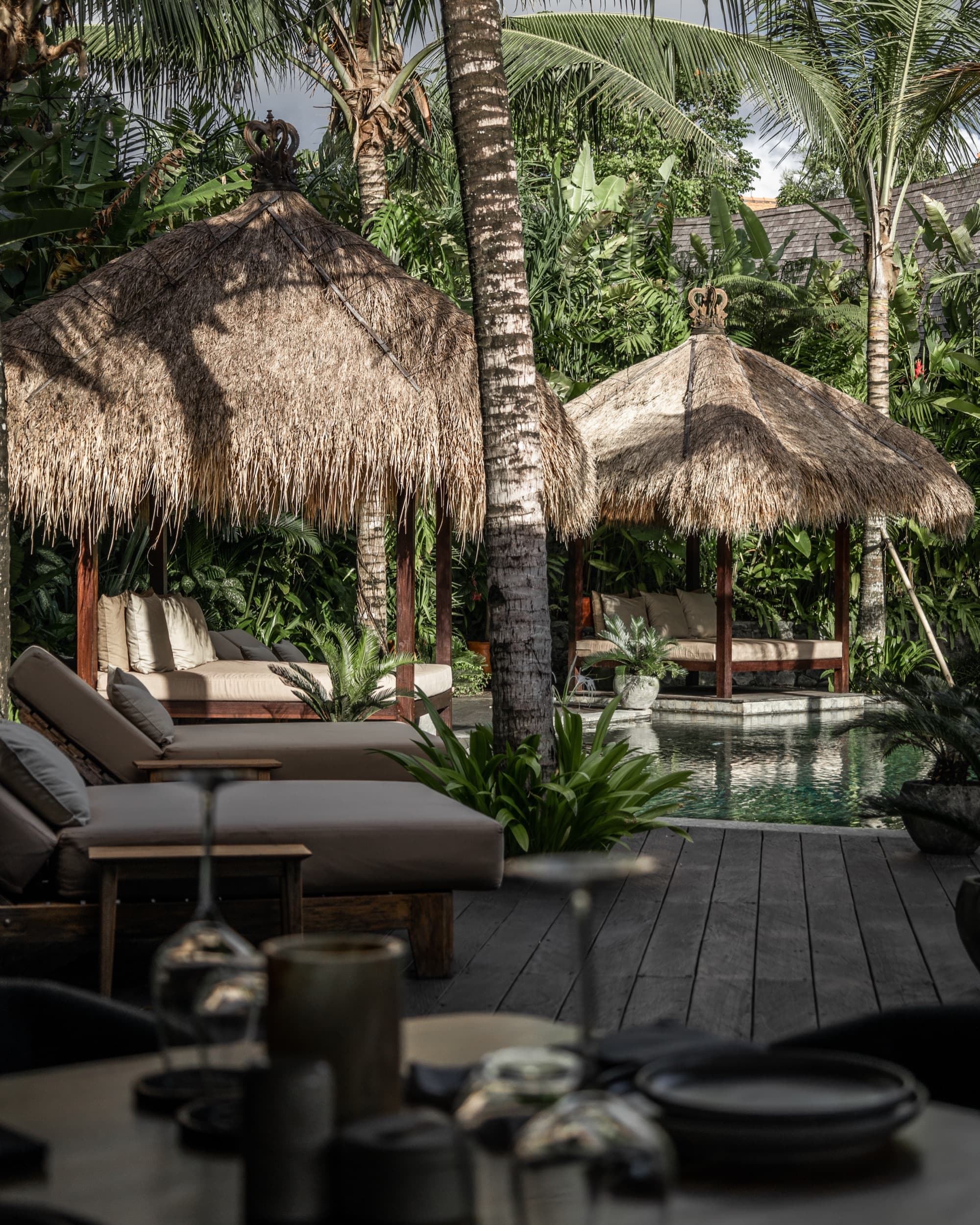 Thatched daybed cabanas and loungers along the timber deck beside the pool