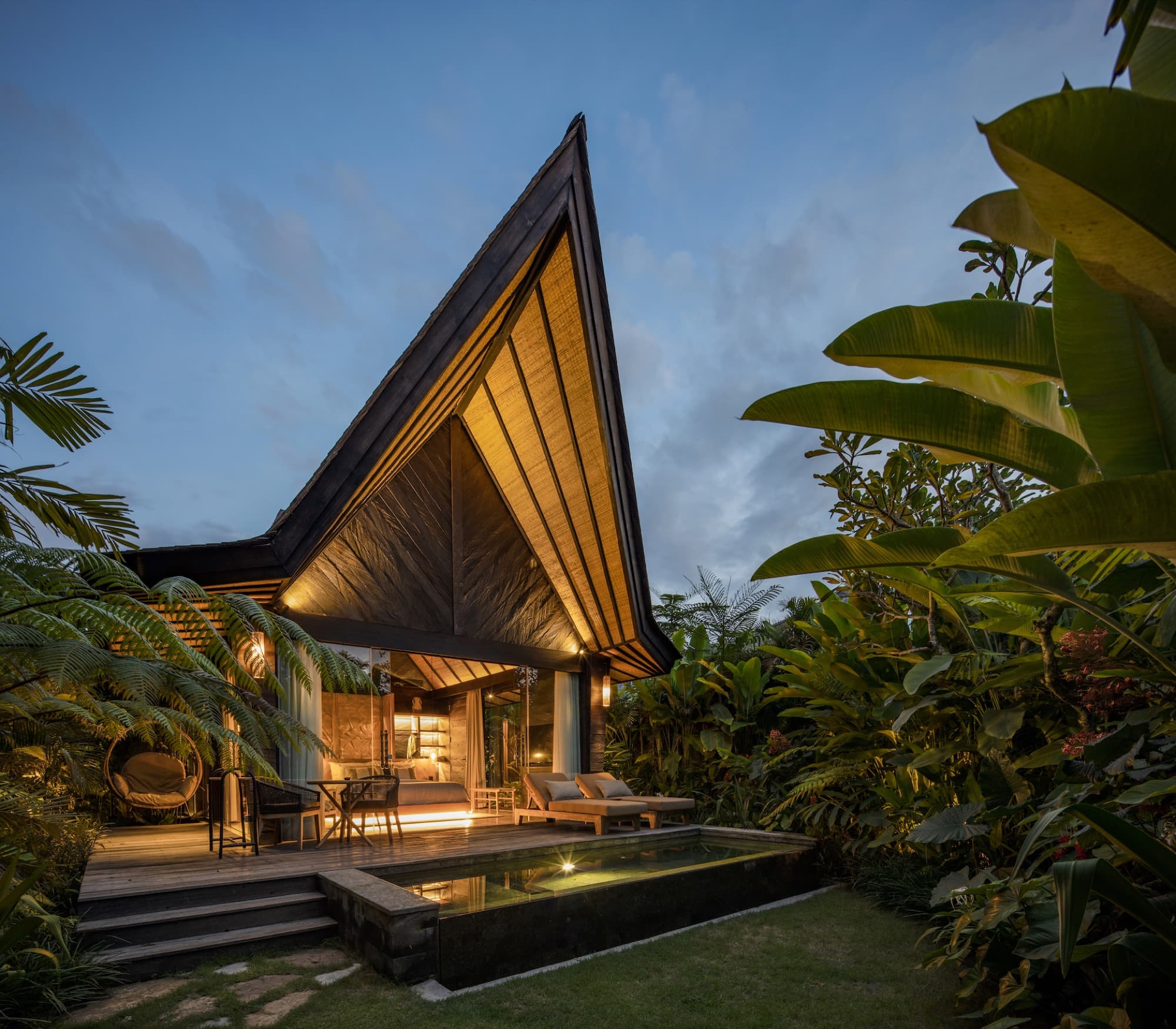 Villa with a steep A-frame roof glowing at dusk above a private plunge pool