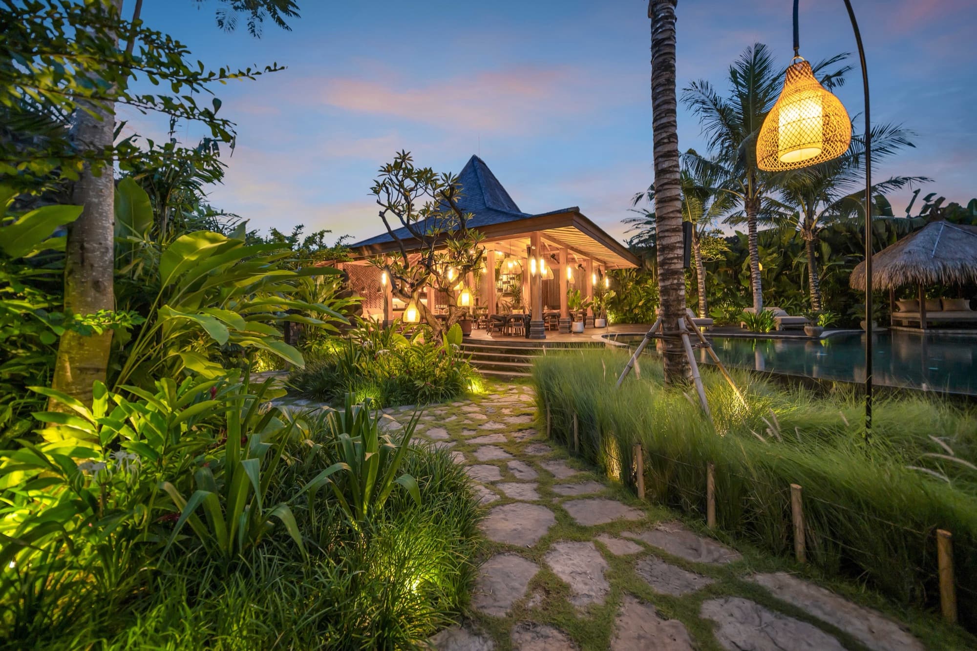 Stone path leading to the lantern-lit Ijo restaurant pavilion beside the pool at dusk