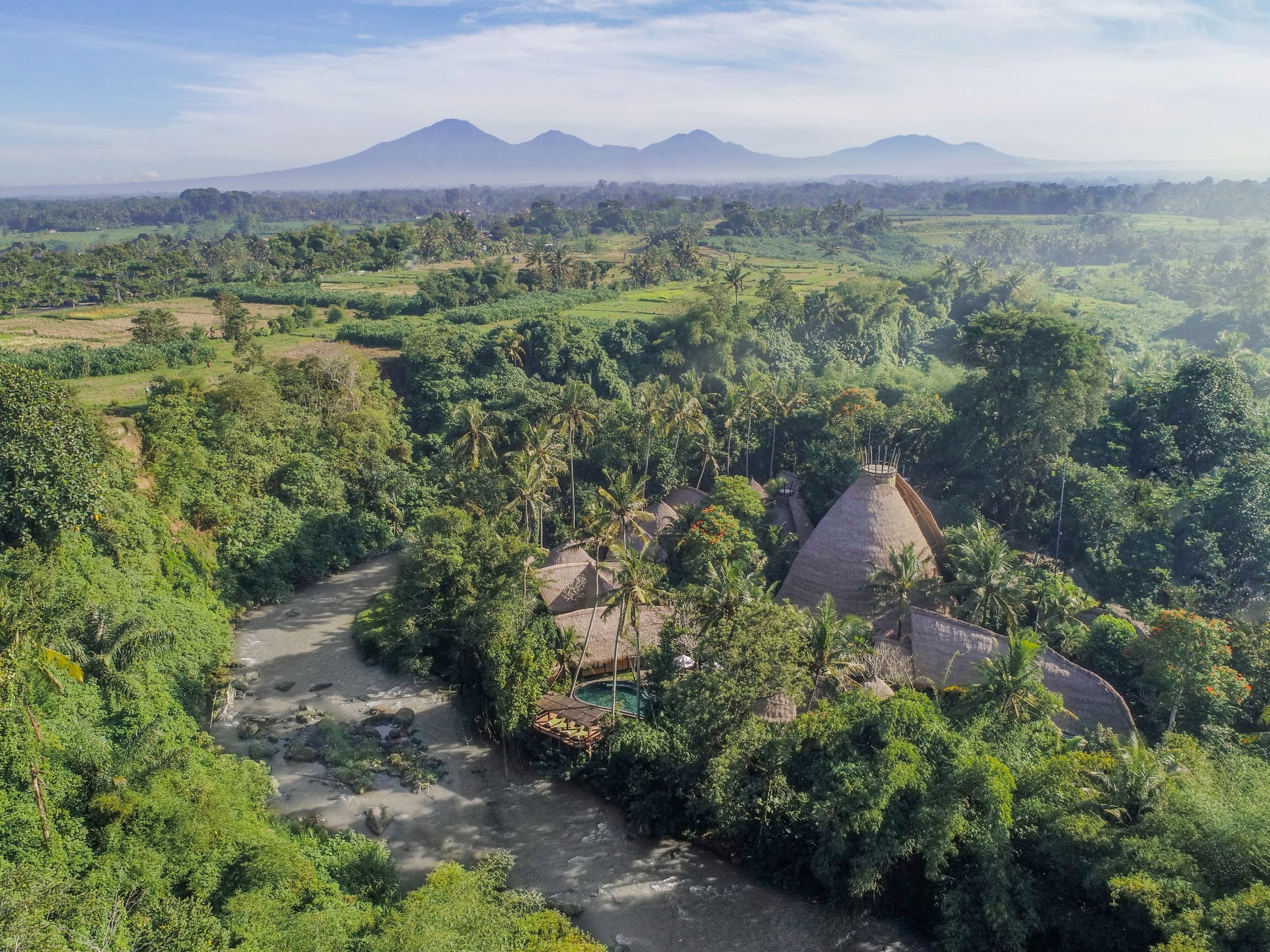 Aerial view of Fivelements Retreat among palm trees with Mount Batur in the distance, Bali