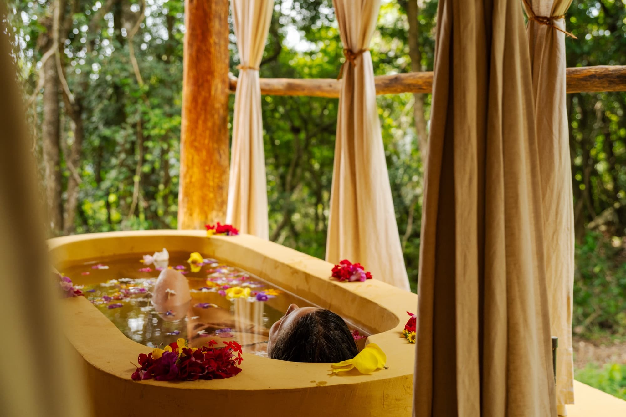 Terracotta bathtub scattered with flower petals overlooking the rainforest