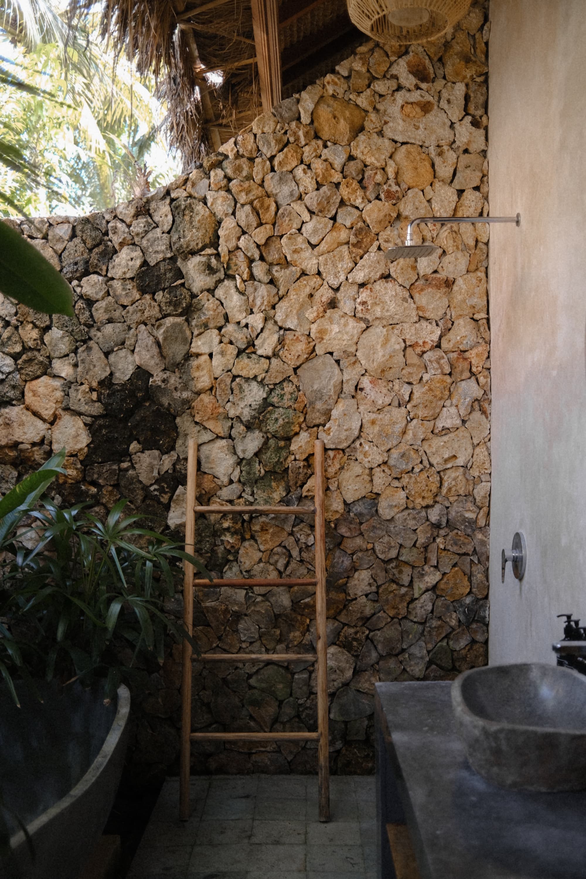 Open-air bathroom with a stone wall, timber ladder and carved stone basin
