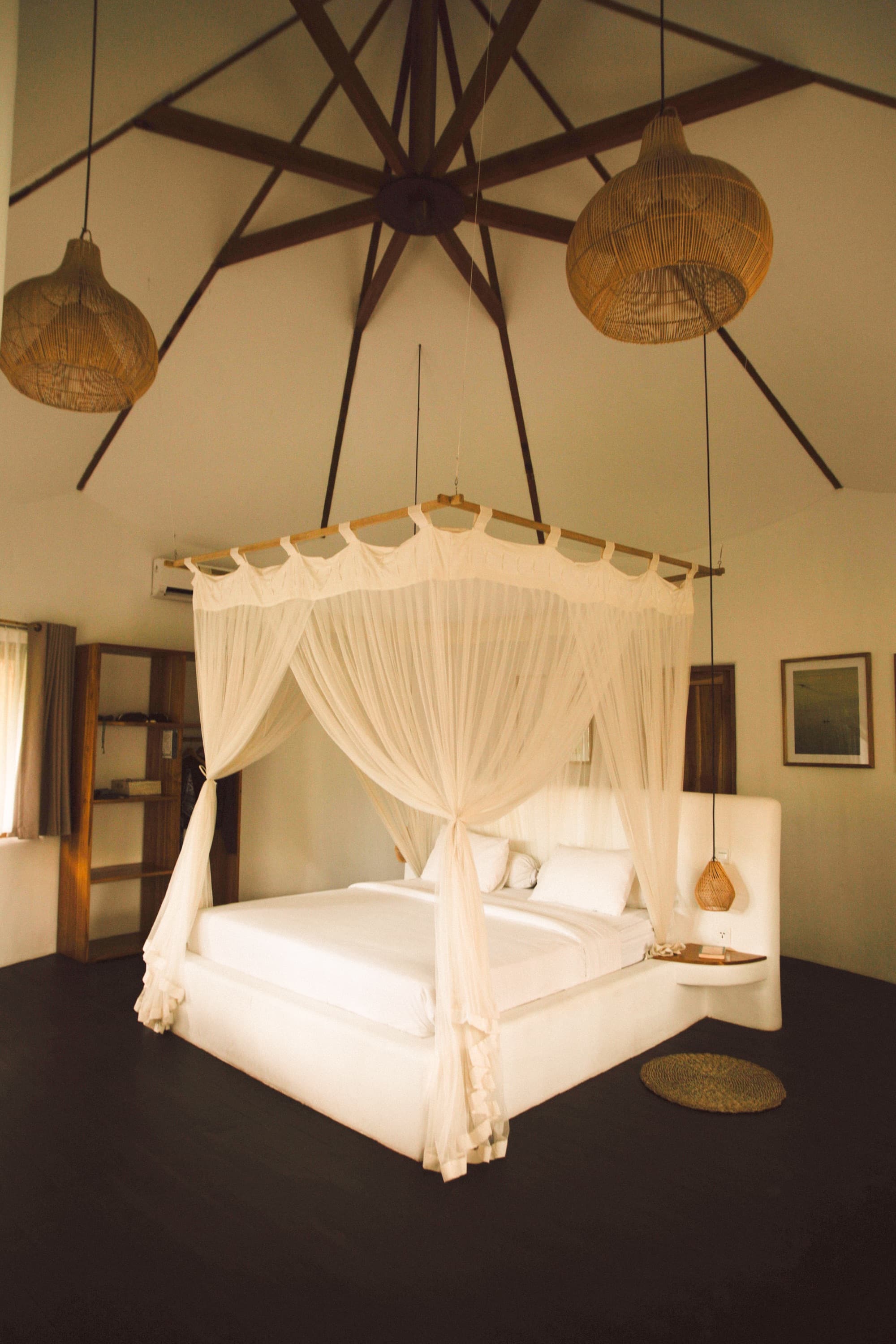 Canopy bed under a high vaulted ceiling with woven rattan pendant lamps