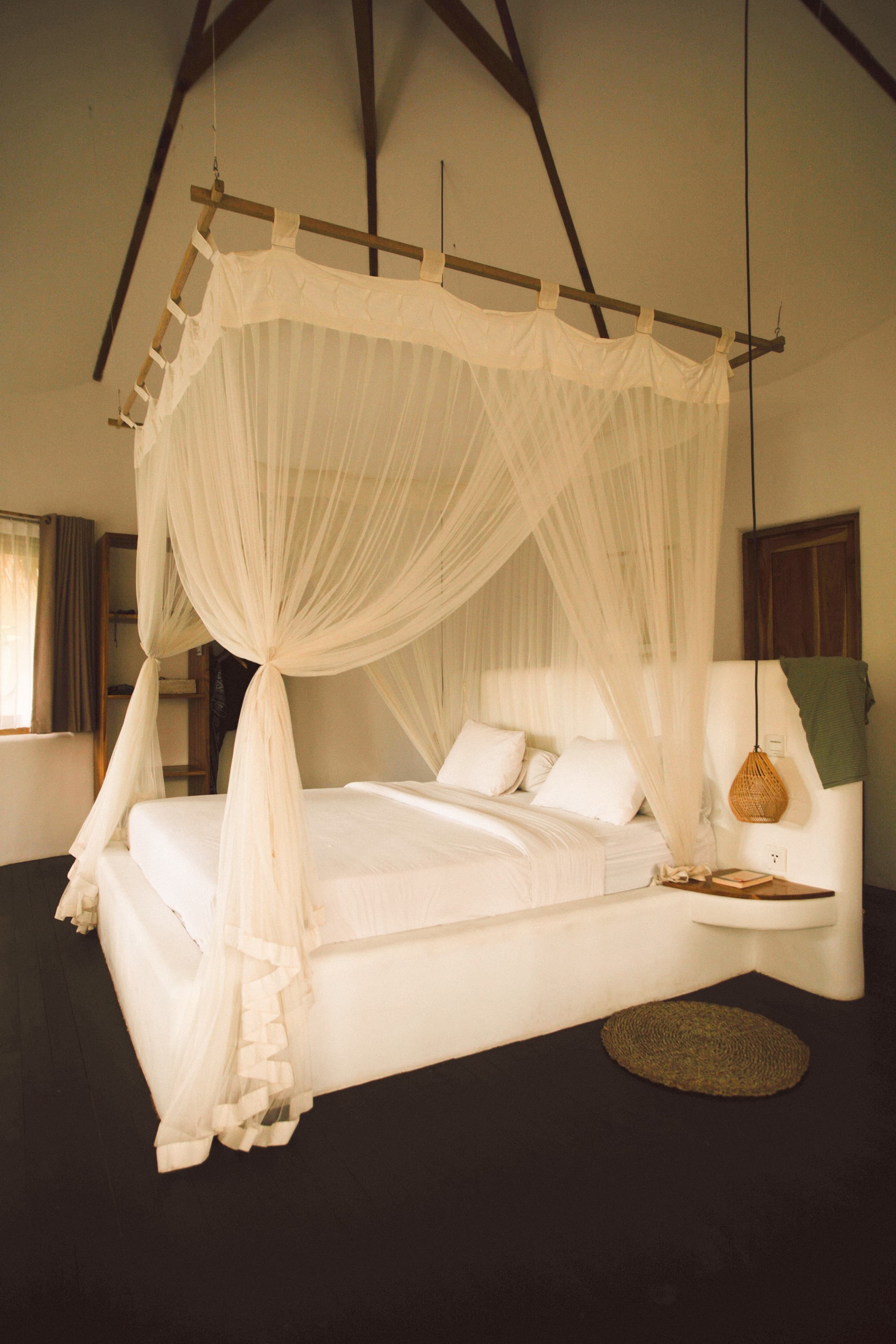 Canopy bed with mosquito net and dark timber floor in a garden room, Mana Eco Retreat, Kuta Lombok