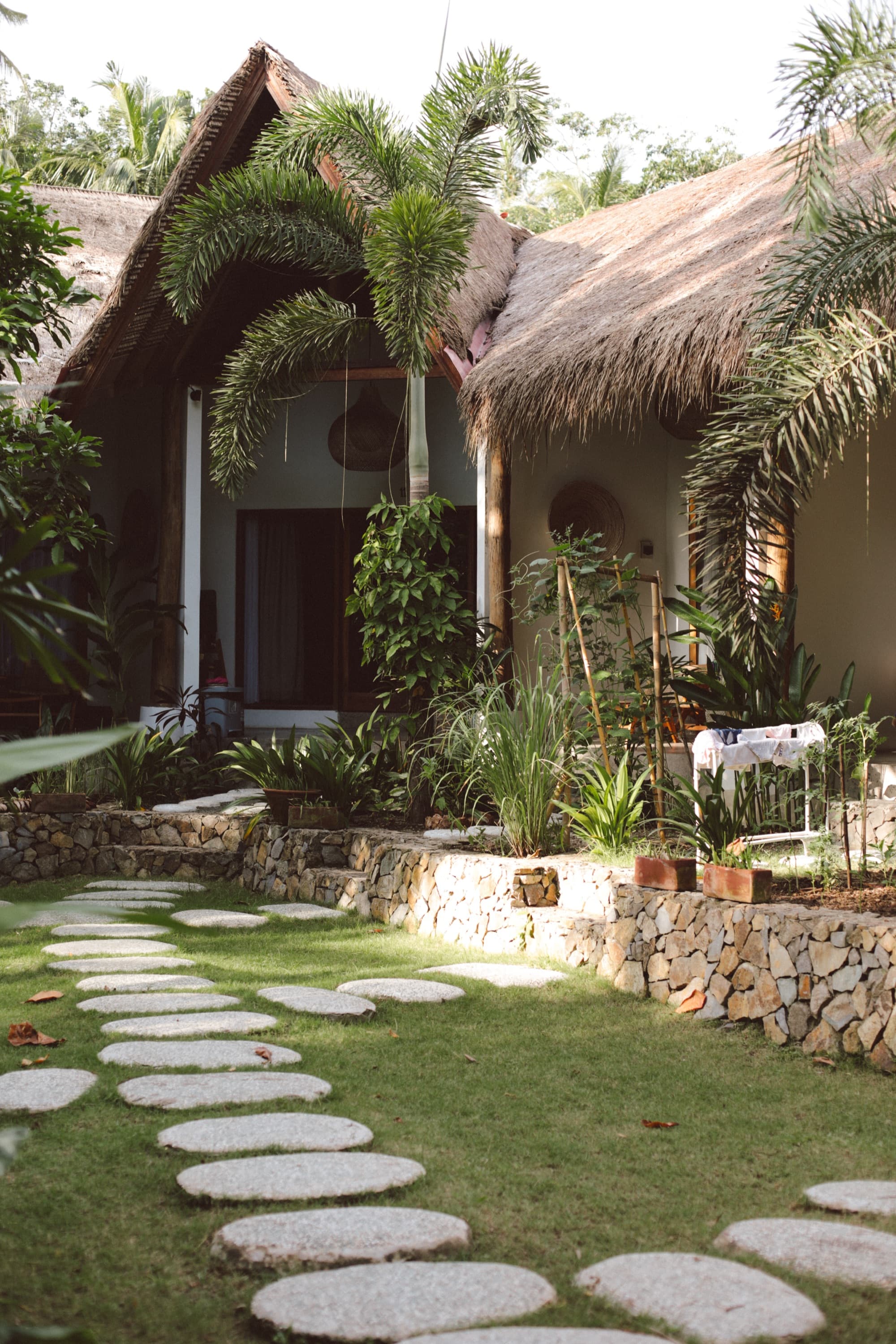 Thatched bungalow behind a dry-stone wall and stepping-stone path through the garden