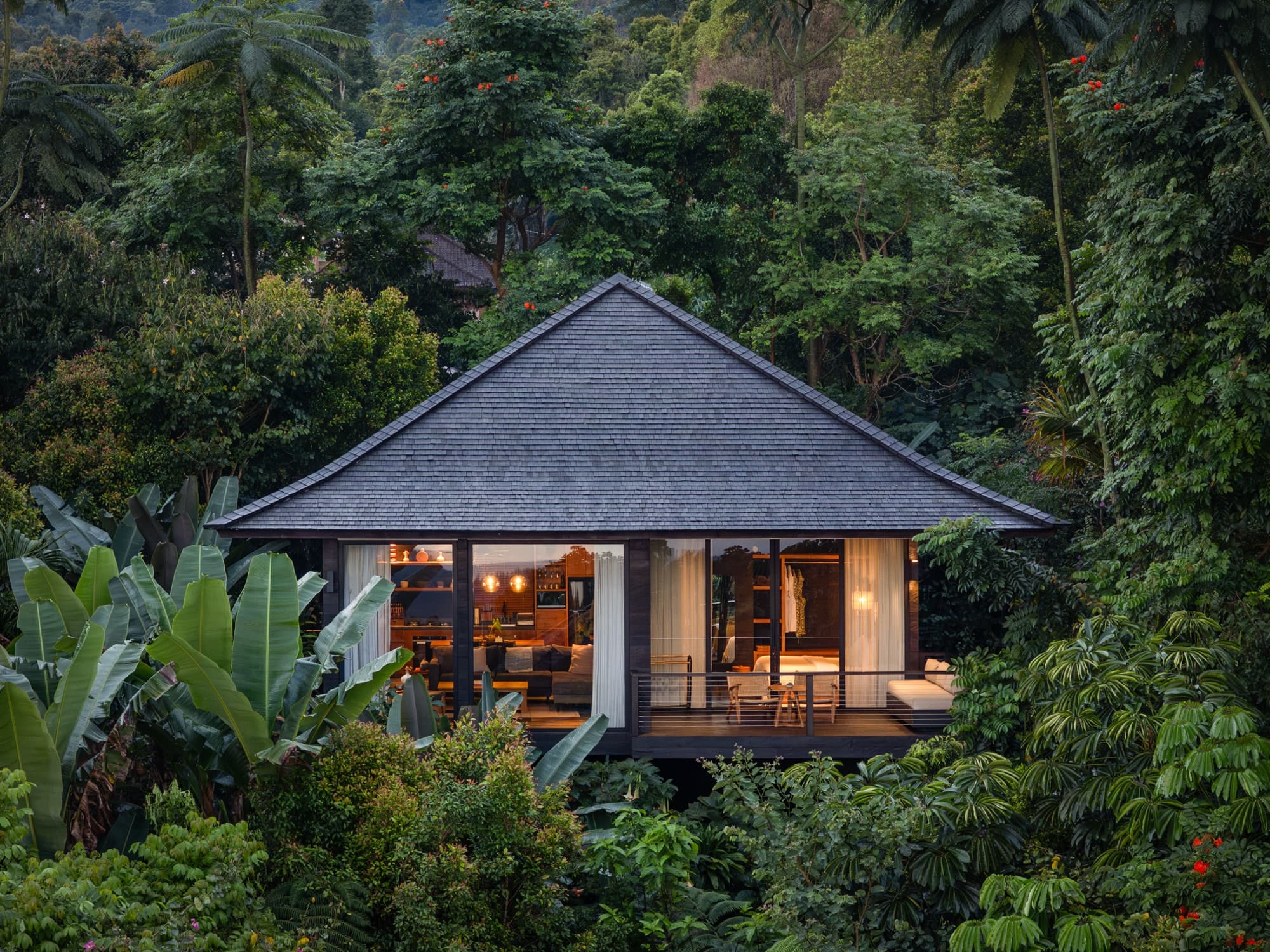 Timber cabin with a shingled roof glowing at dusk, surrounded by rainforest in Munduk, North Bali