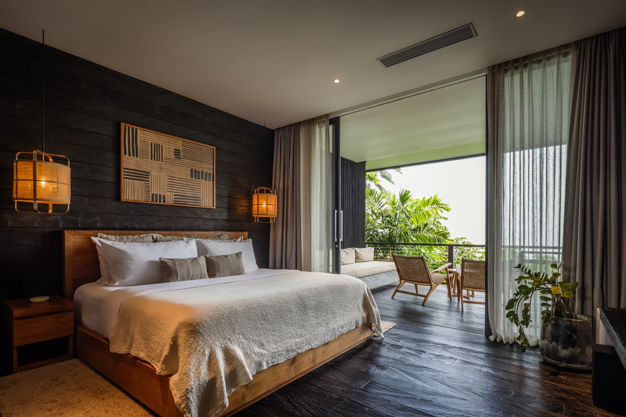 Cabin bedroom with a king bed, dark timber wall and sliding doors opening to a jungle balcony
