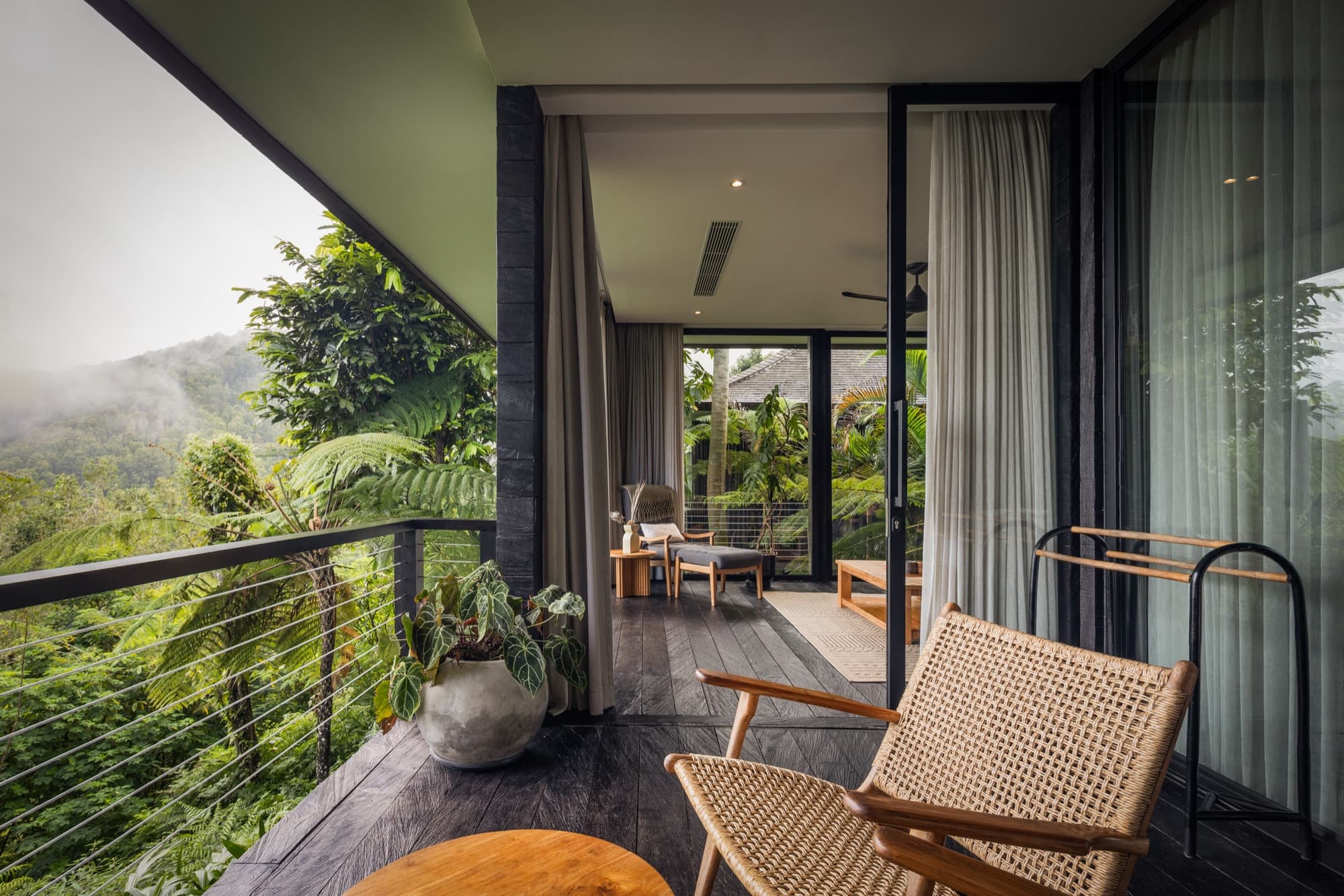 Cabin balcony with rattan chairs facing forested mountains wrapped in mist