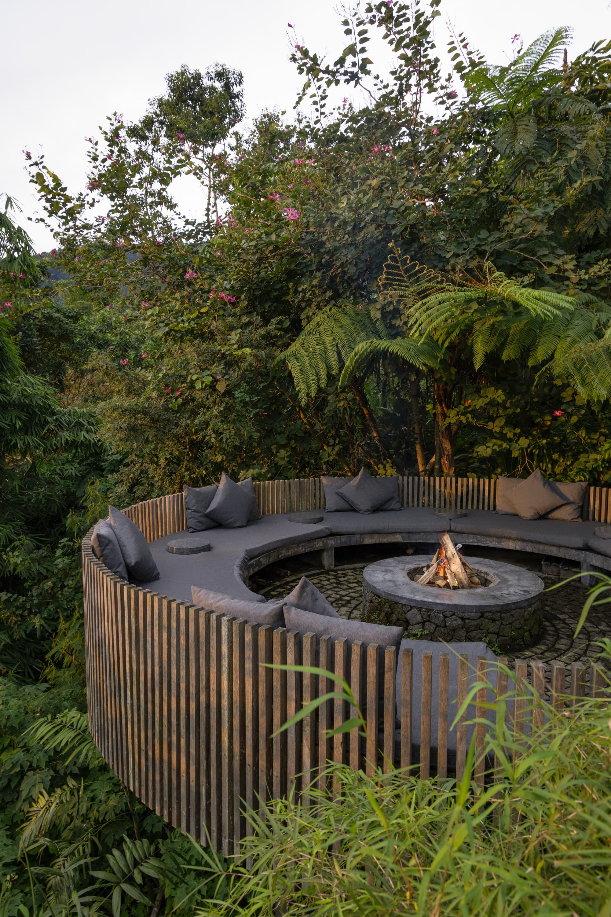 Circular sunken firepit lounge with cushioned seating ringed by rainforest