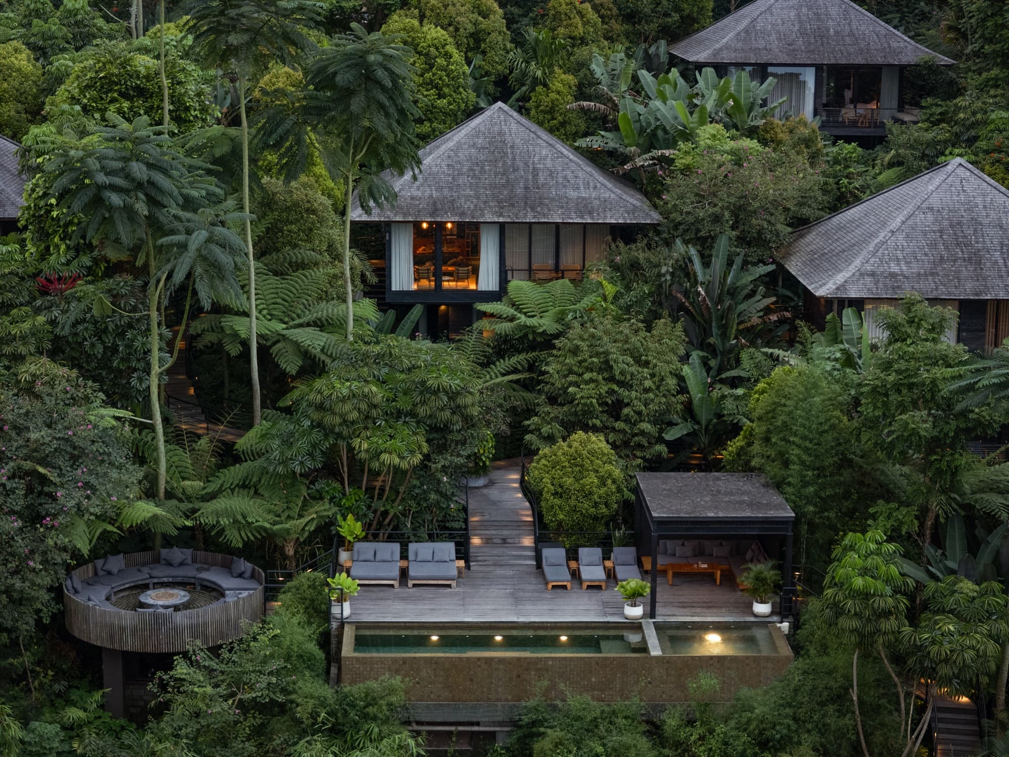 Aerial view of the cabins, a pool deck with loungers and a round firepit set in the jungle