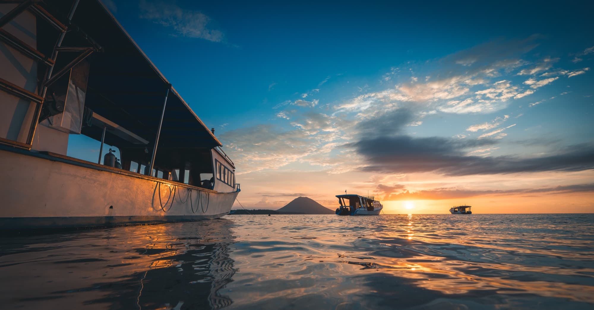 A dive boat on the water at sunset with Manado Tua on the horizon
