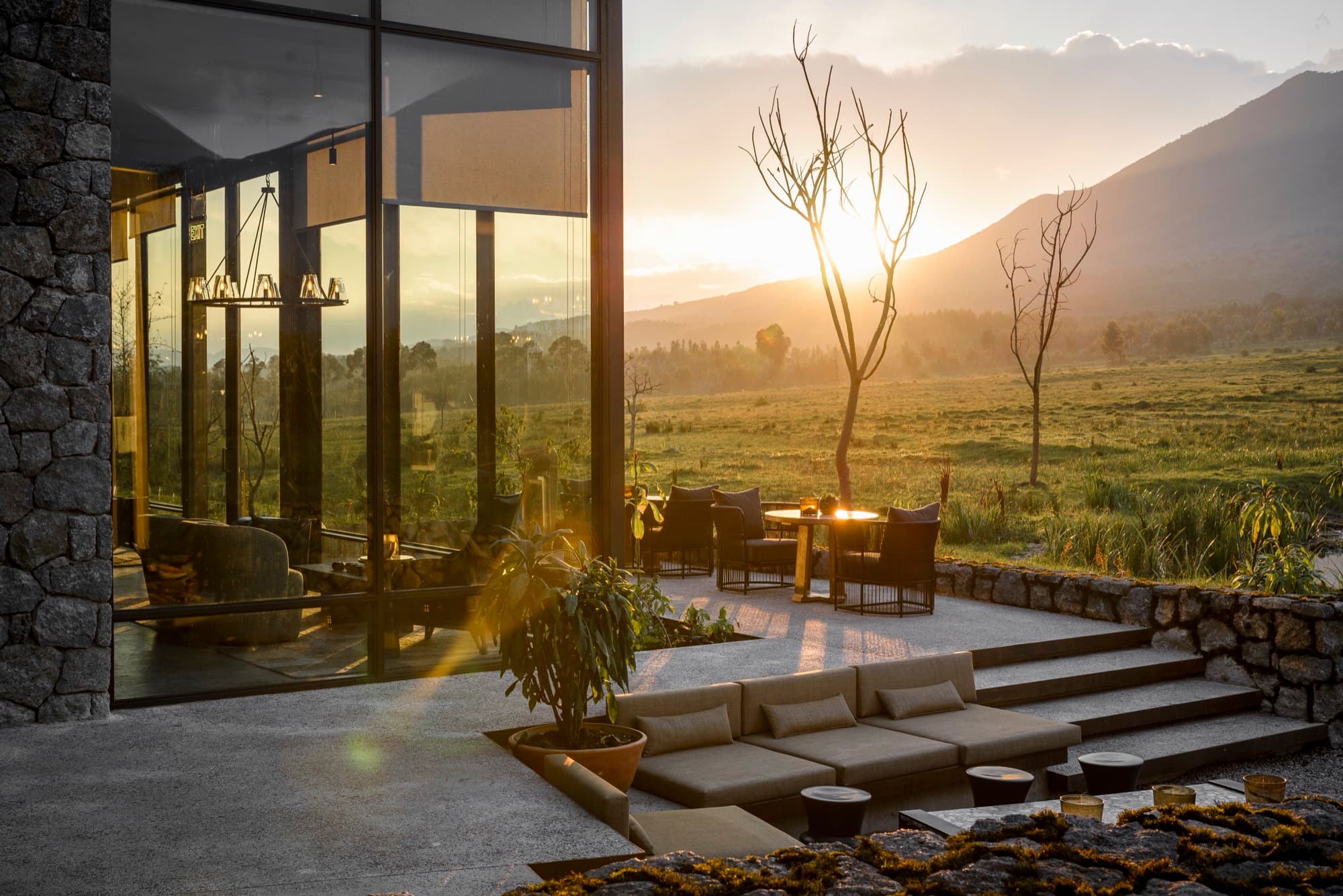 Glass-walled lodge building and sunken terrace at sunset, volcano behind